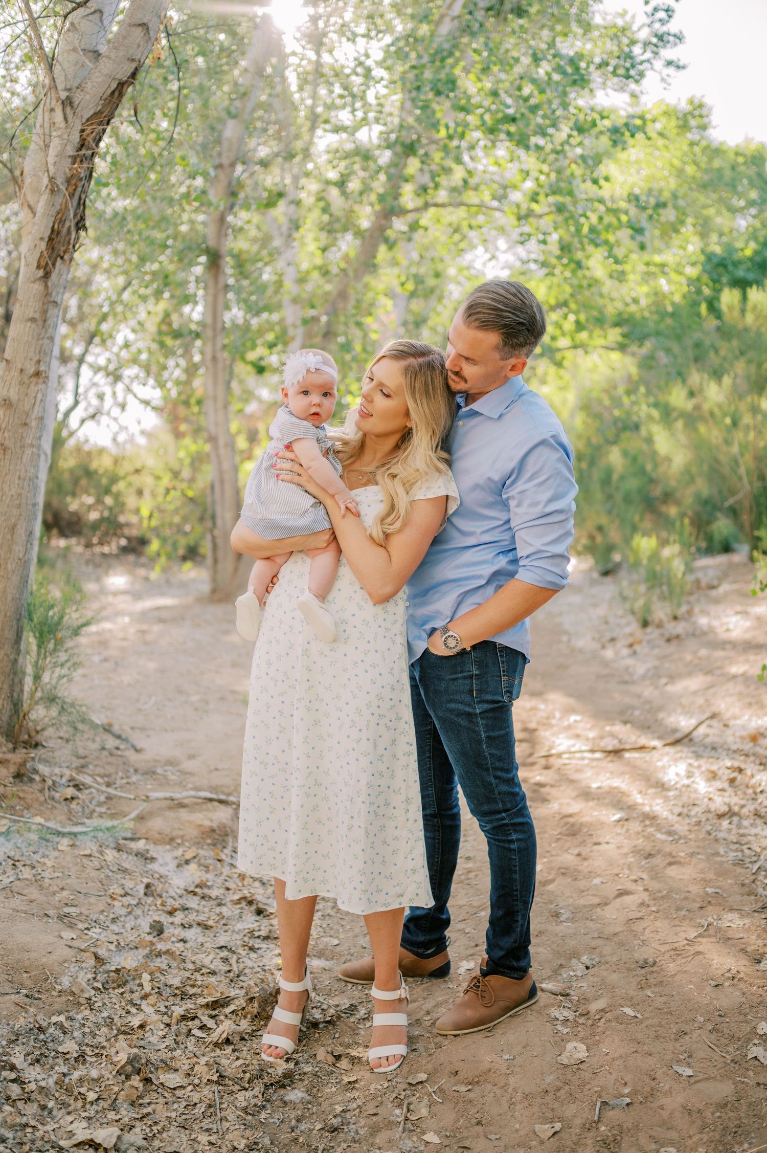 A family shares tender moments together on a dirt path surrounded by trees in warm natural lighting. Phoenix Arizona family photographer.