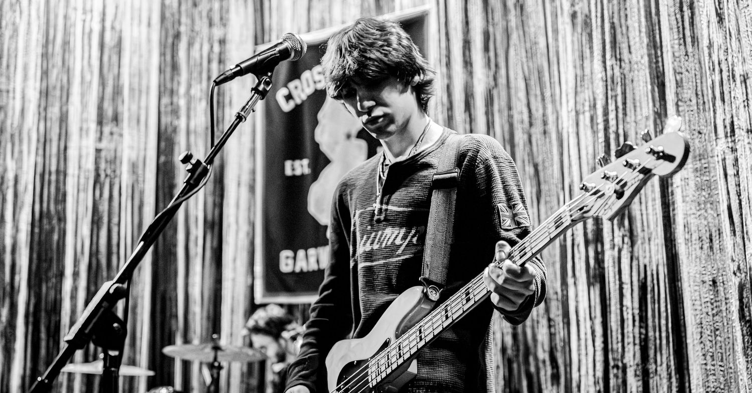 Young male bassist performing on stage in black and white, standing before a microphone.