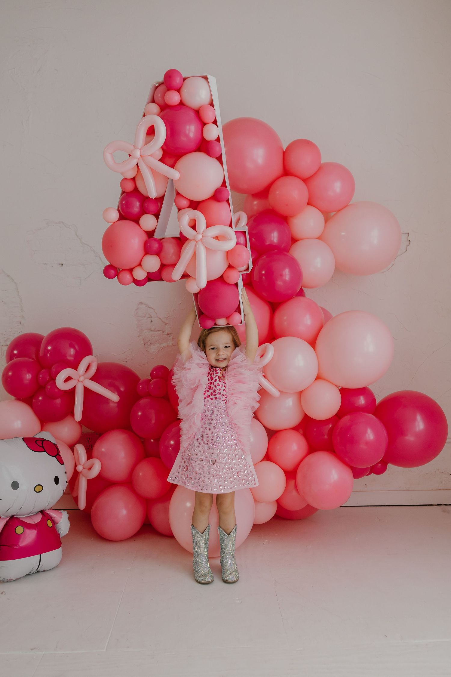 Child in pink tutu dress posing in front of pink balloon arch display.