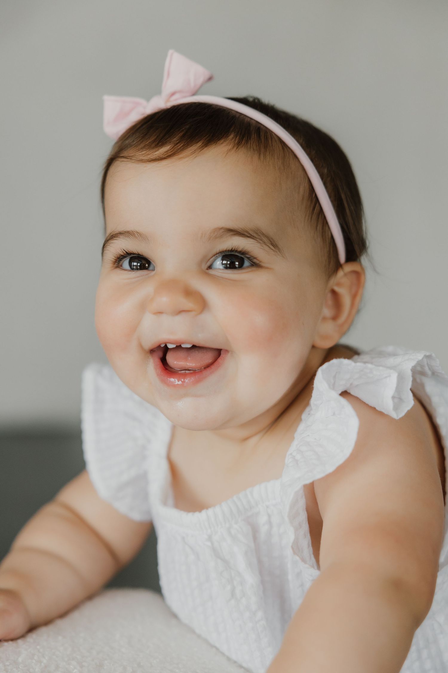 Baby wearing white dress and headband smiles during portrait session.