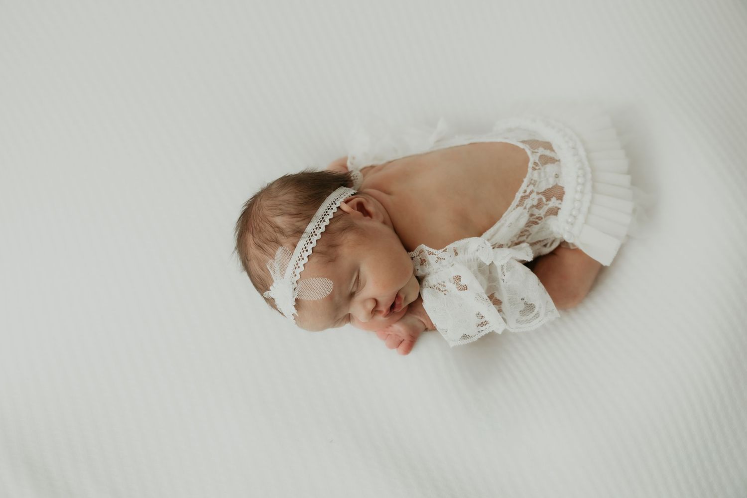 Newborn baby sleeping peacefully in white wrap against light background.