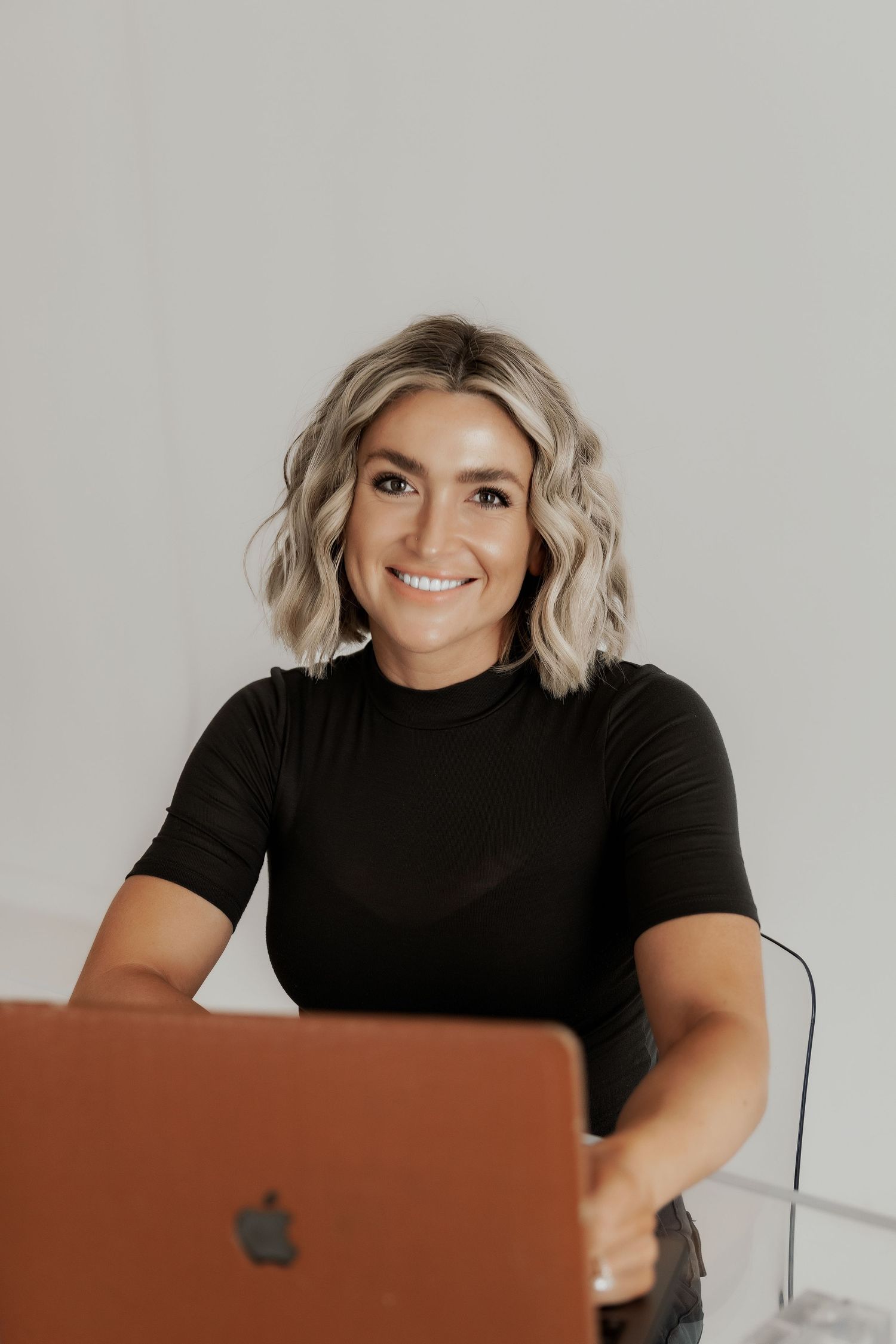 Professional photographer smiling while working behind laptop in studio setting.