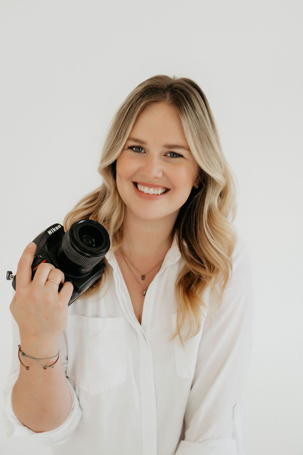 Photographer in white button-down holding professional camera against white background.