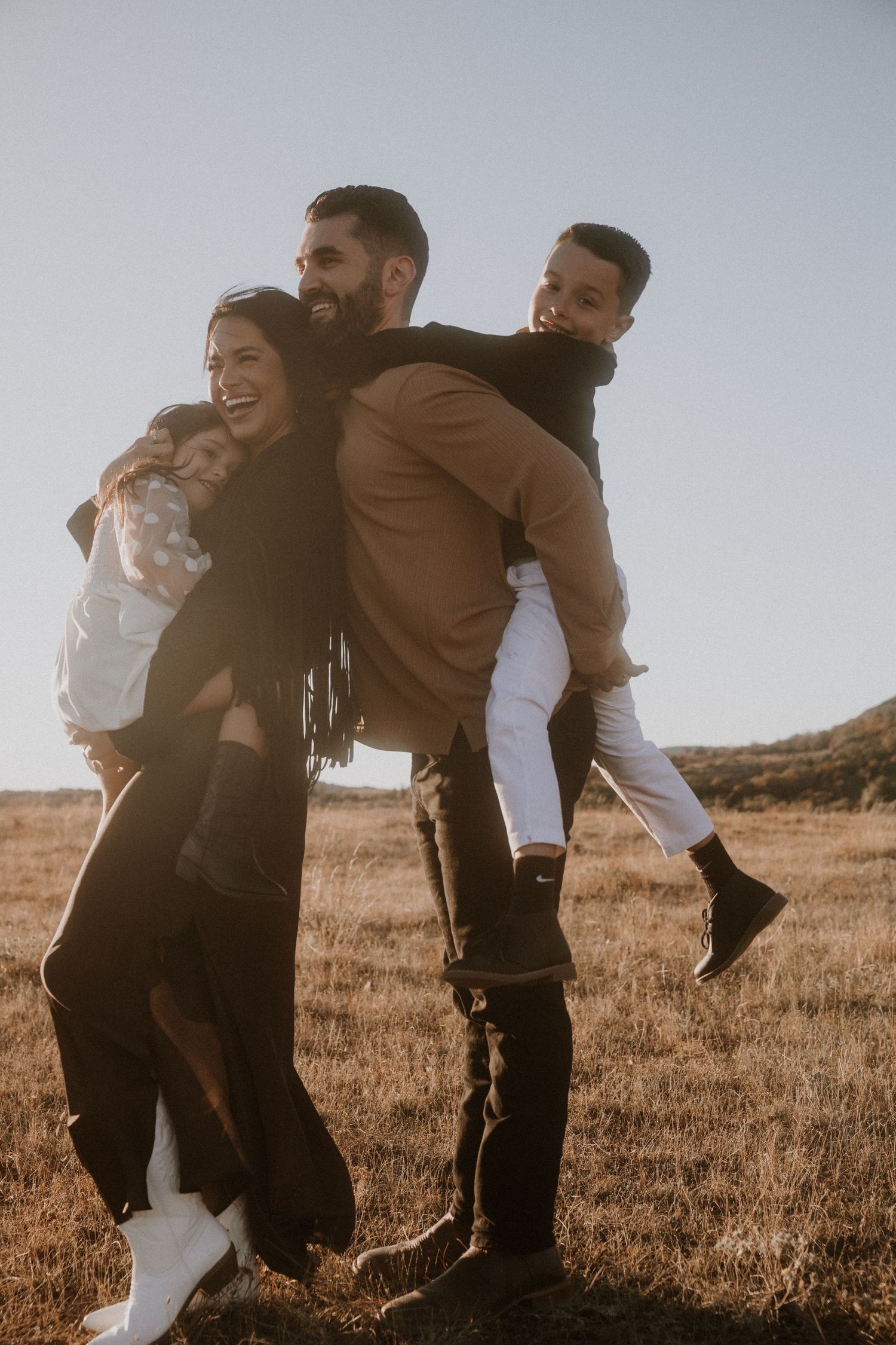 Candid family moments captured in golden sunlight on grassy hillside.