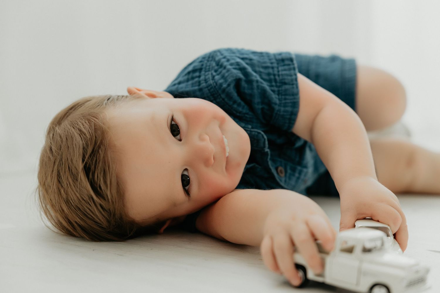 Young child lying down while playing with a white toy car.