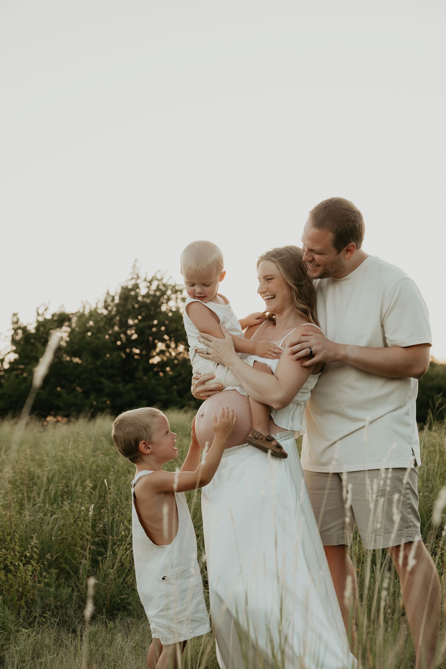 A family shares tender moments together in a sunlit field wearing coordinated white and cream outfits.