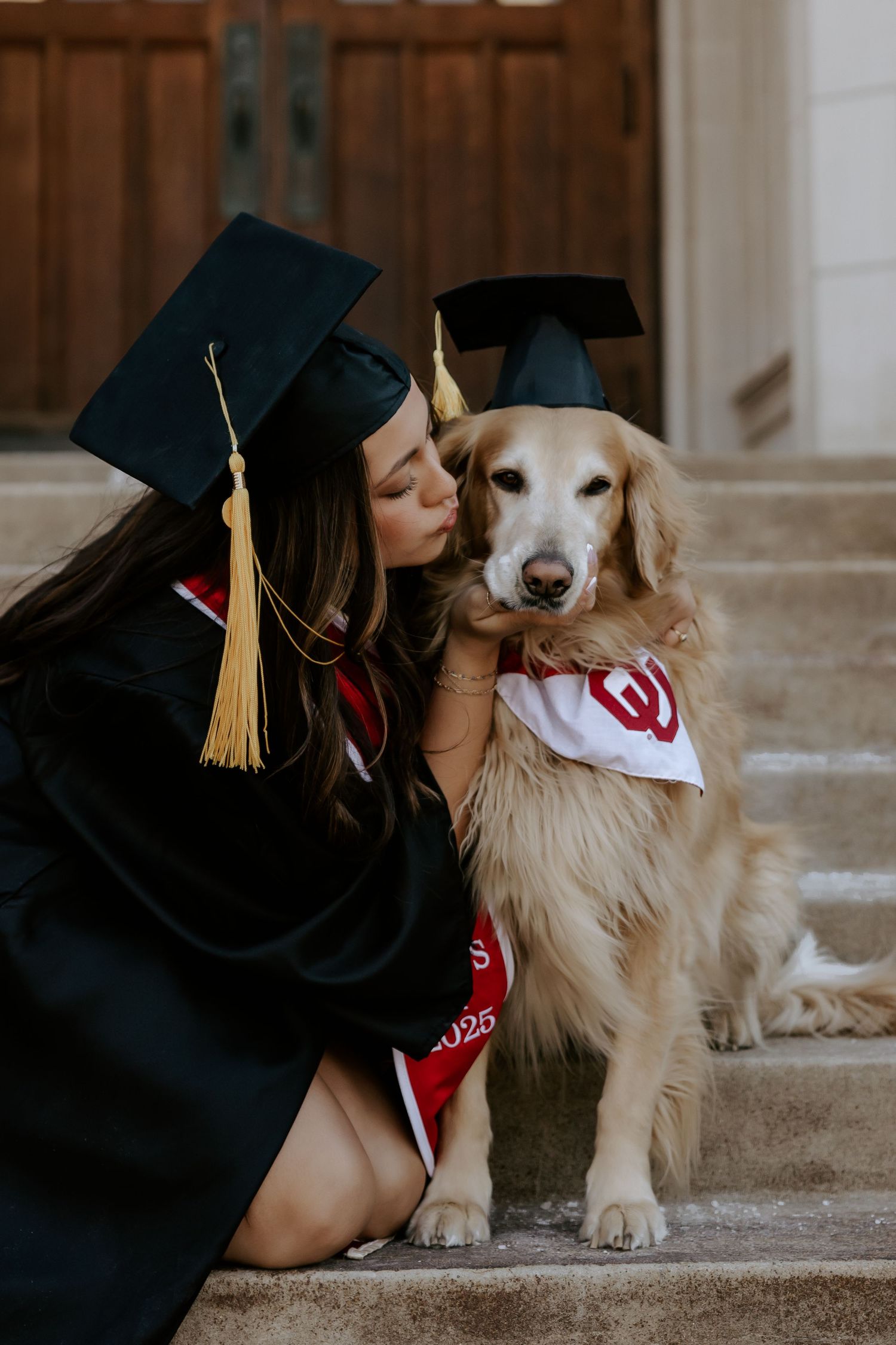 Graduate in cap and gown shares a sweet moment with their Golden Retriever wearing graduation attire.