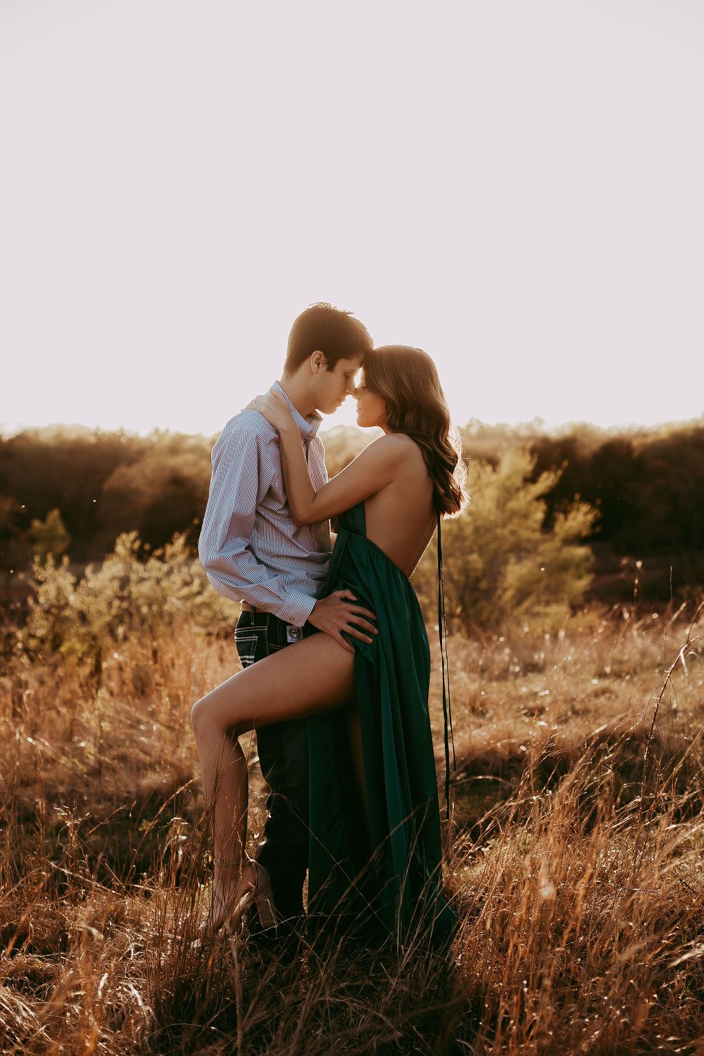Couple embracing in golden field during sunset photoshoot.