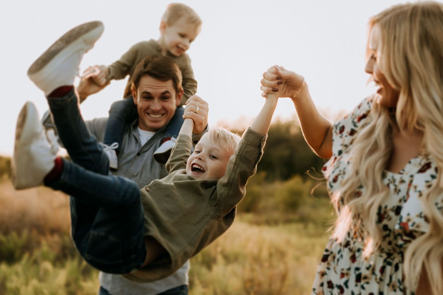 Family playing and dancing together in field during golden hour.