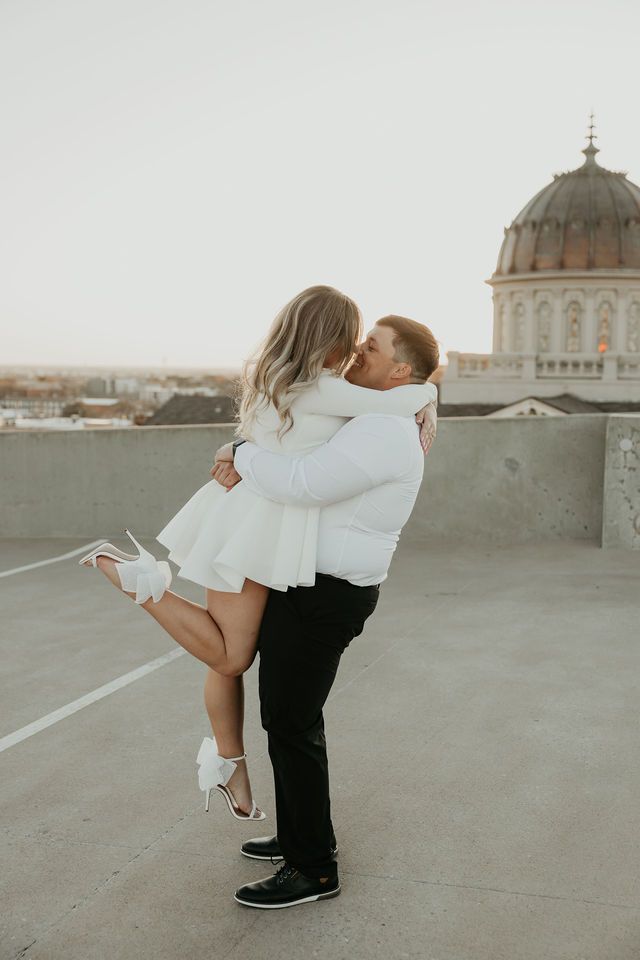 Couple in white clothing sharing romantic moment with domed building in background.