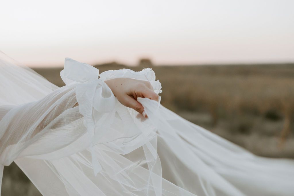 Ethereal white wedding dress flowing in a scenic outdoor setting at sunset.