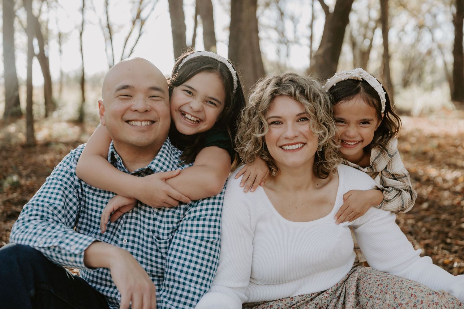 Family sitting together on fallen autumn leaves in a wooded setting.