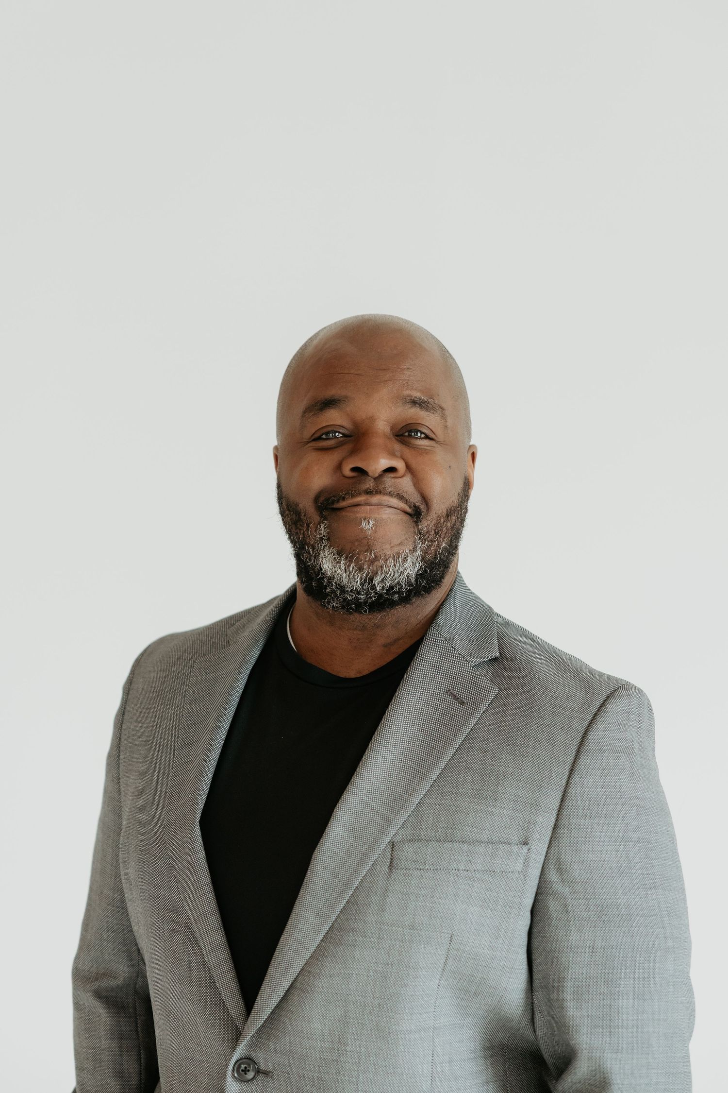Professional headshots of person in gray suit jacket and black shirt against white background.