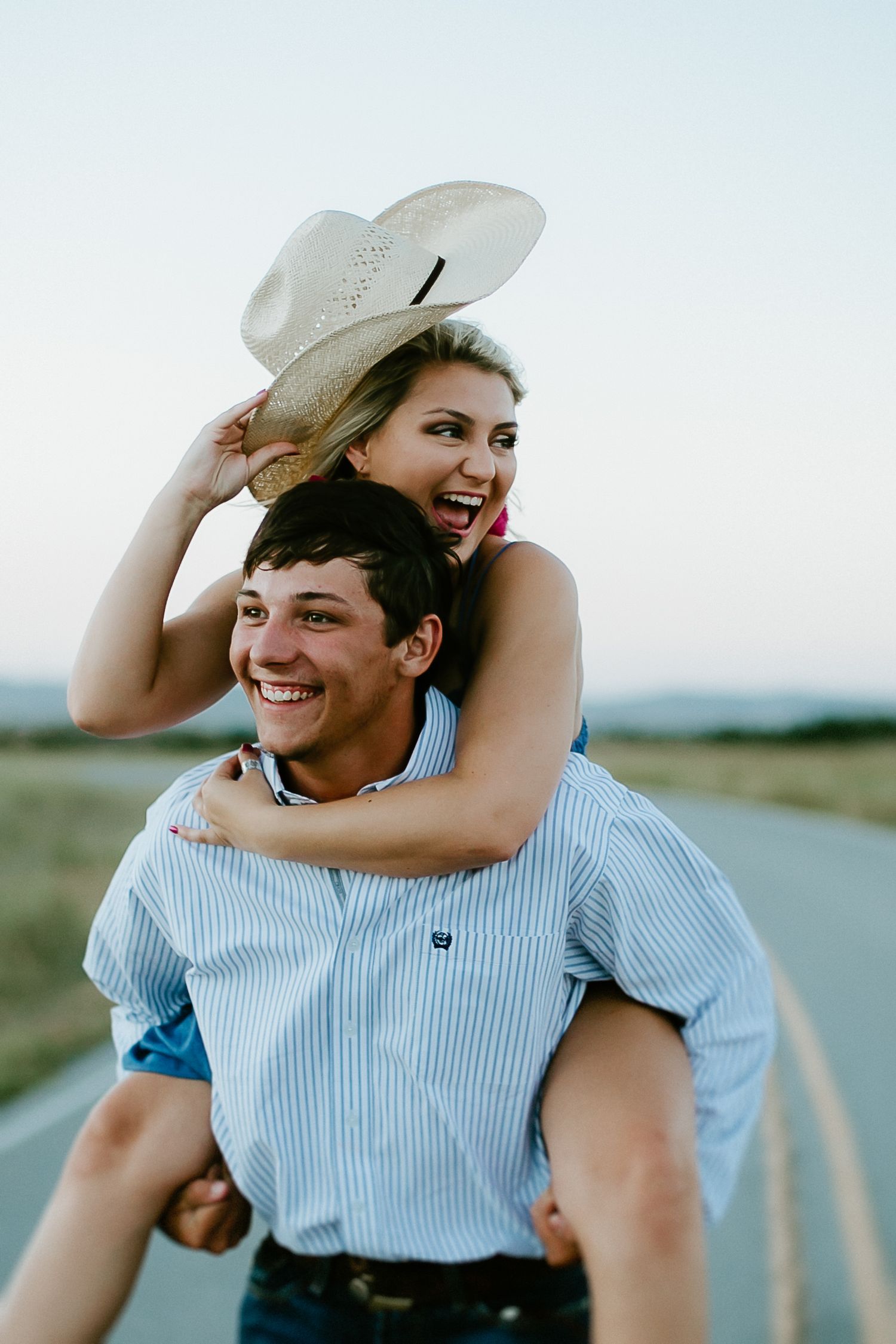 Playful couple in western attire sharing joyful moments outdoors.