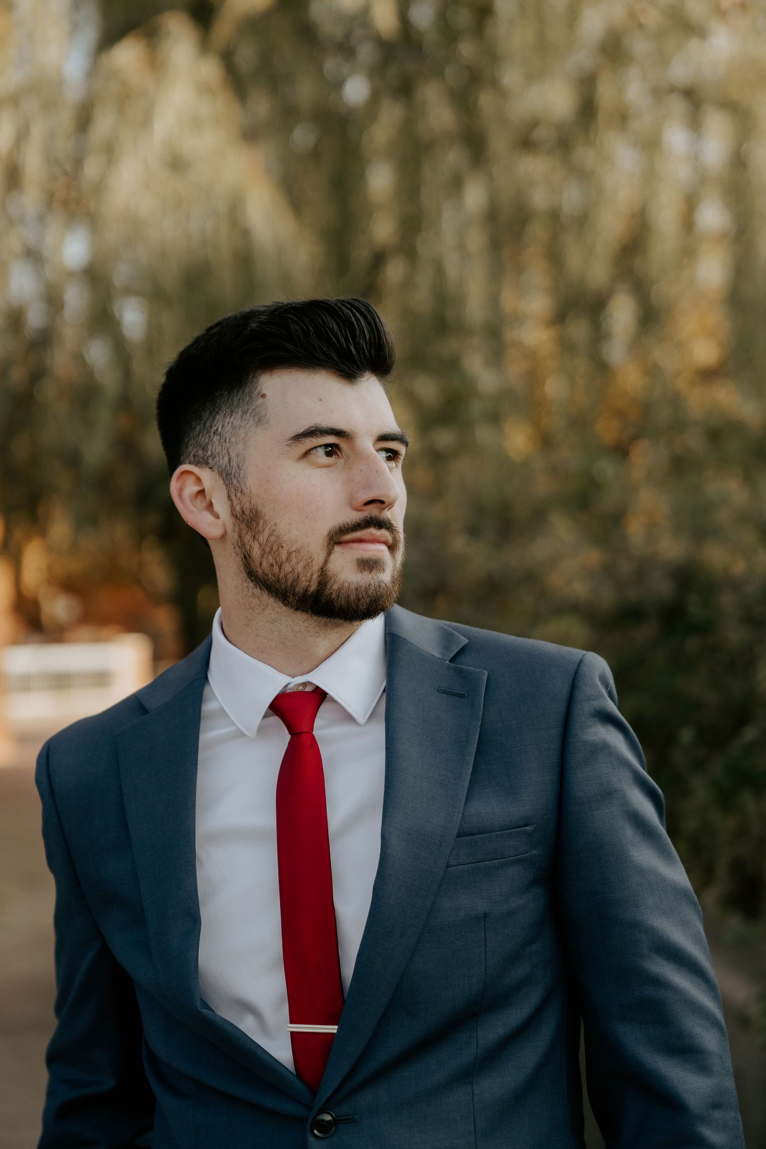 Graduate in navy suit and red tie poses for professional headshots outdoors.