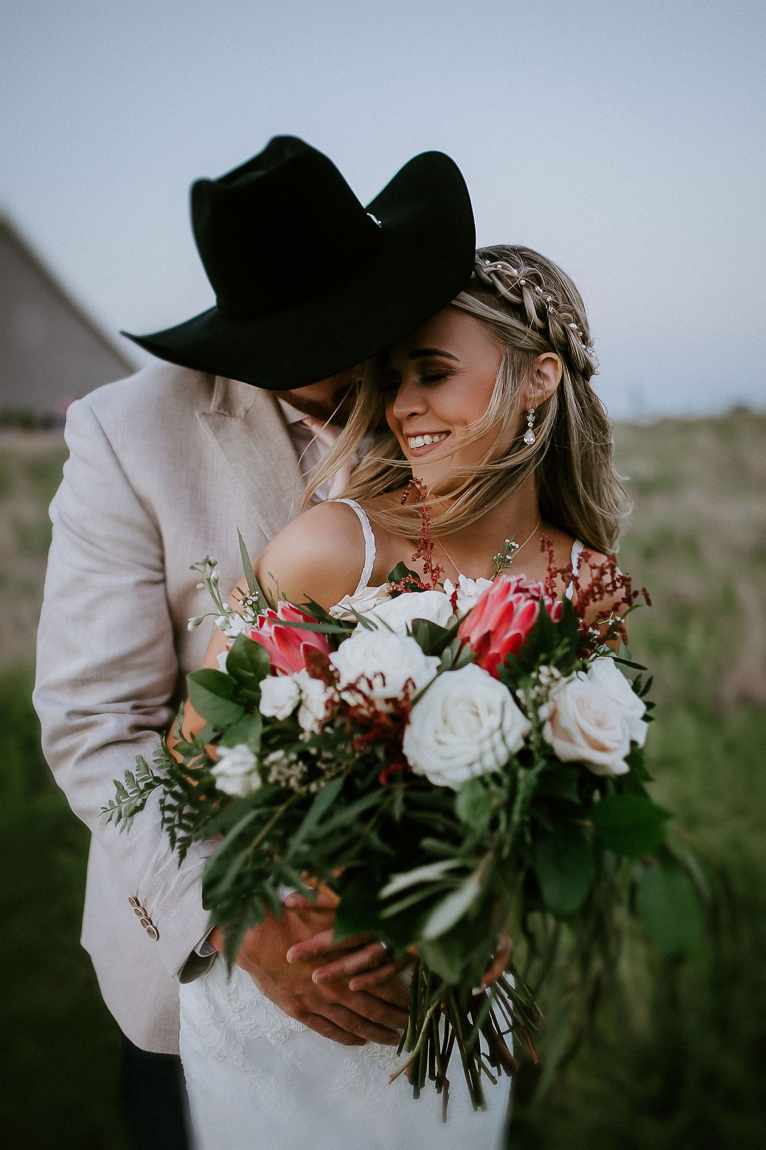 A romantic wedding couple embraces while holding a bouquet of pink and white roses.