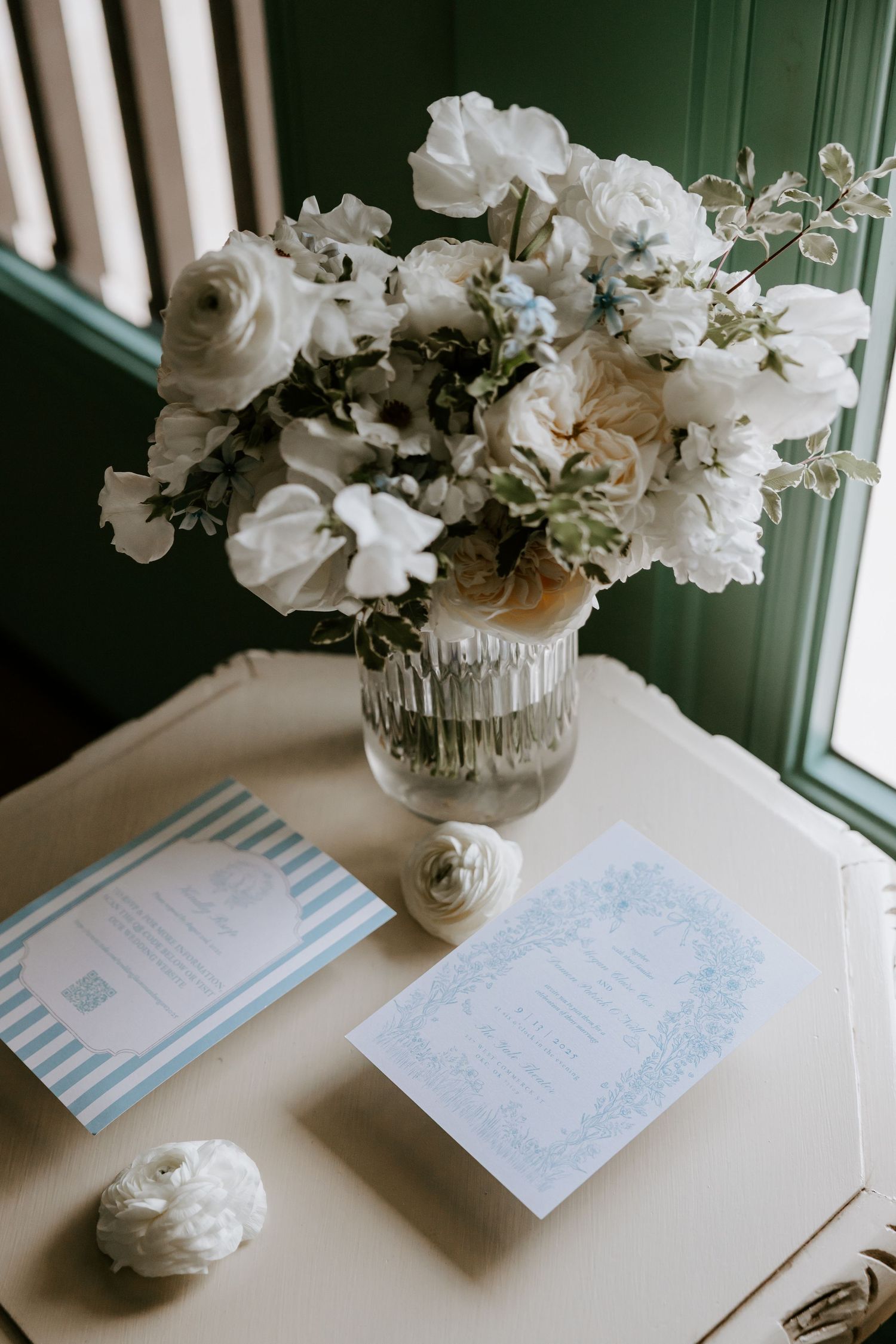 Wedding stationery and white floral centerpiece on table by window.