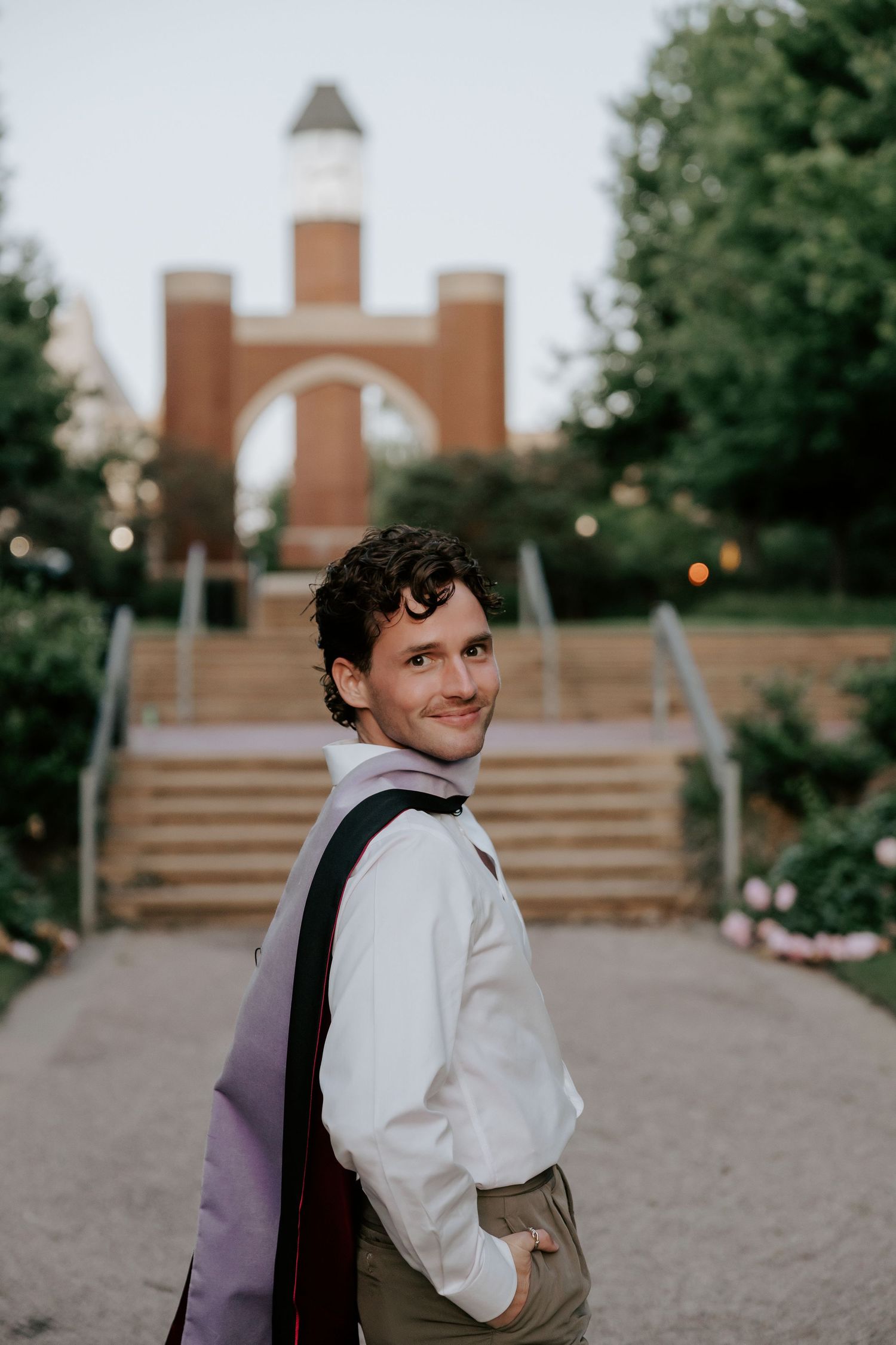 Person in white and dark clothing turns to smile at camera outdoors.