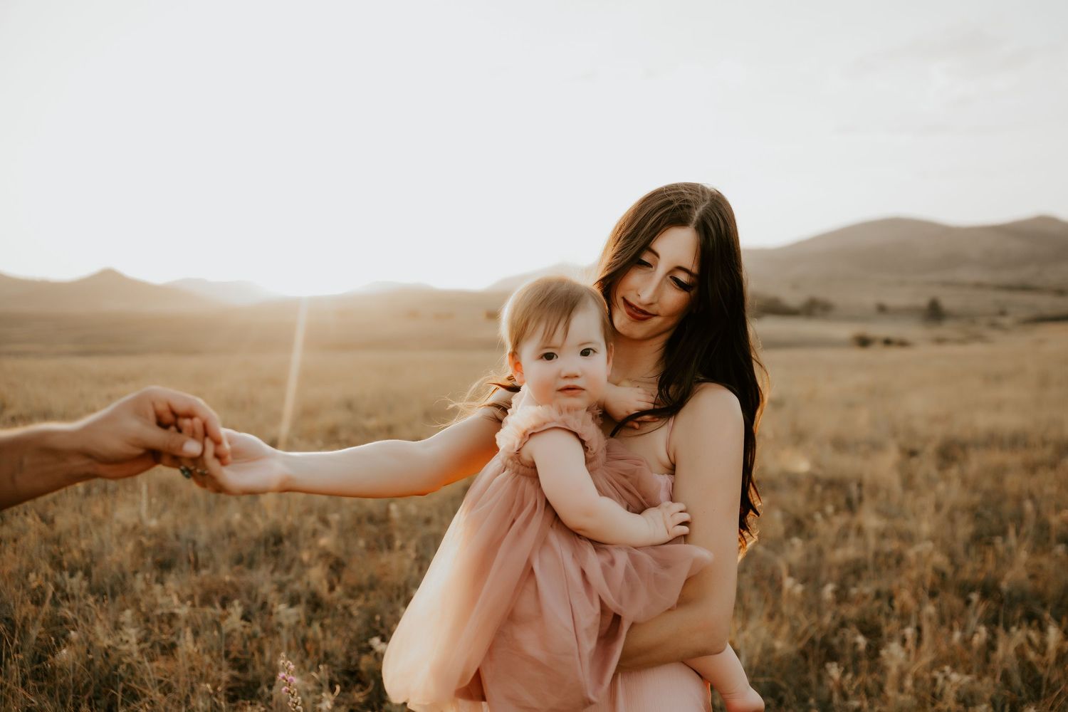 Family sharing tender moments in field during sunset golden hour.