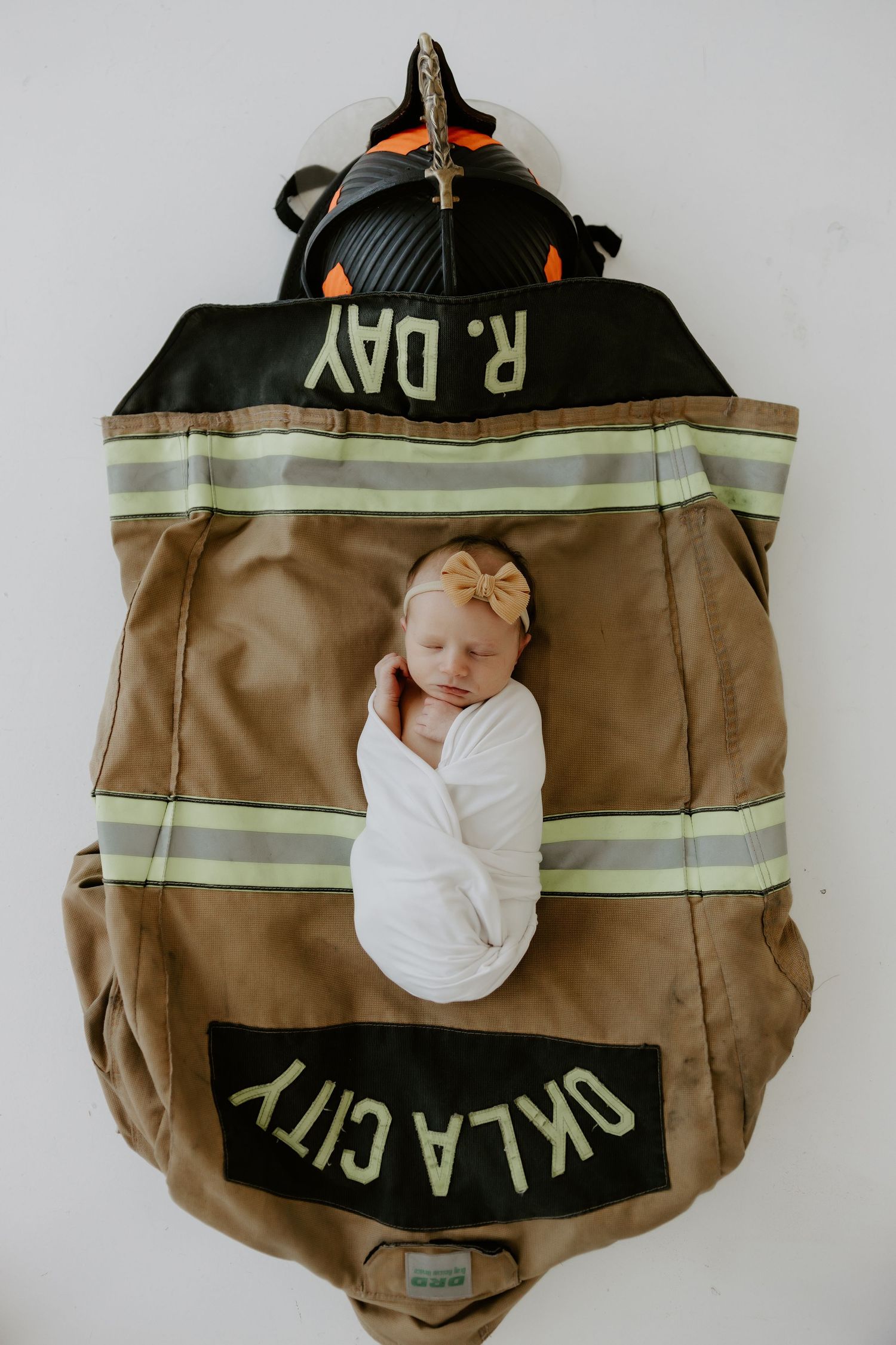 Sleeping newborn in white wrap nestled in firefighter turnout gear with reflective stripes.