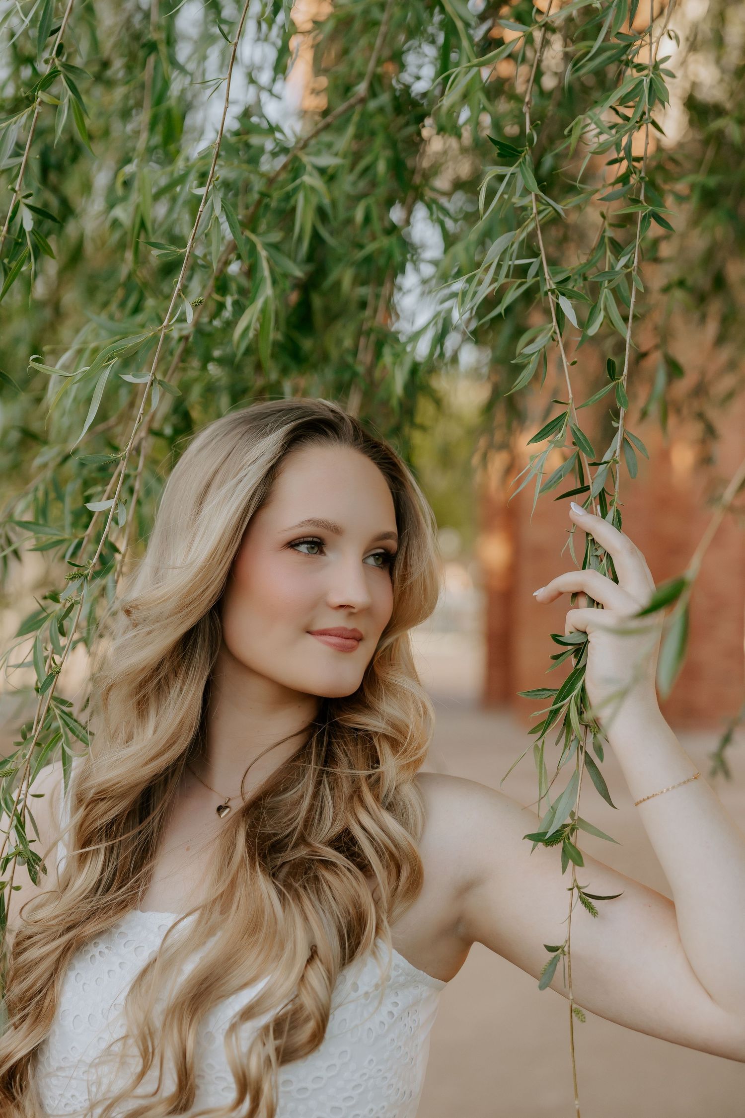 Willow tree branches frame outdoor portrait against brick building.