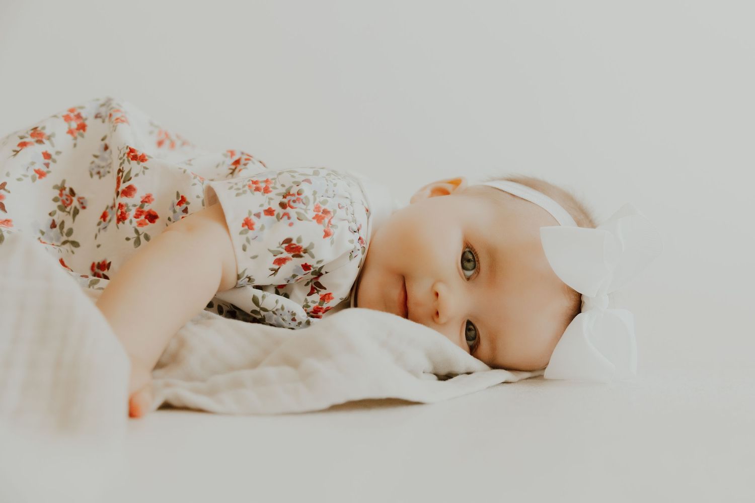 Baby resting peacefully on light colored bedding with floral pattern.