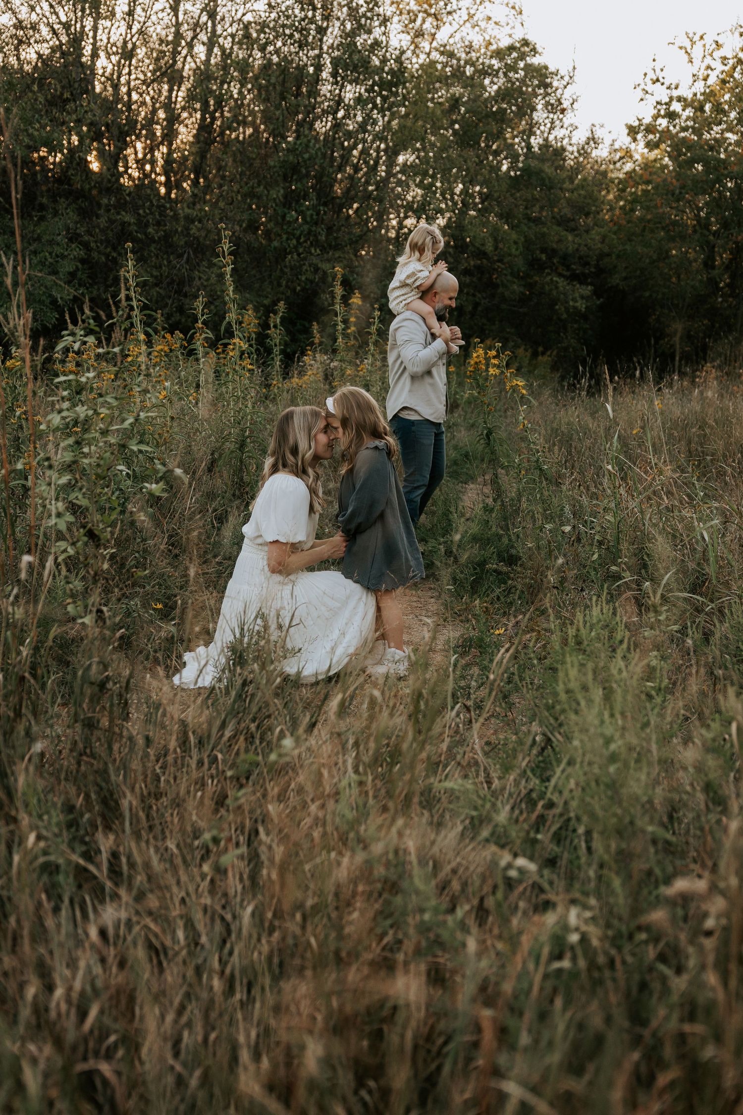 Family plays together in tall grass field during golden hour photoshoot.