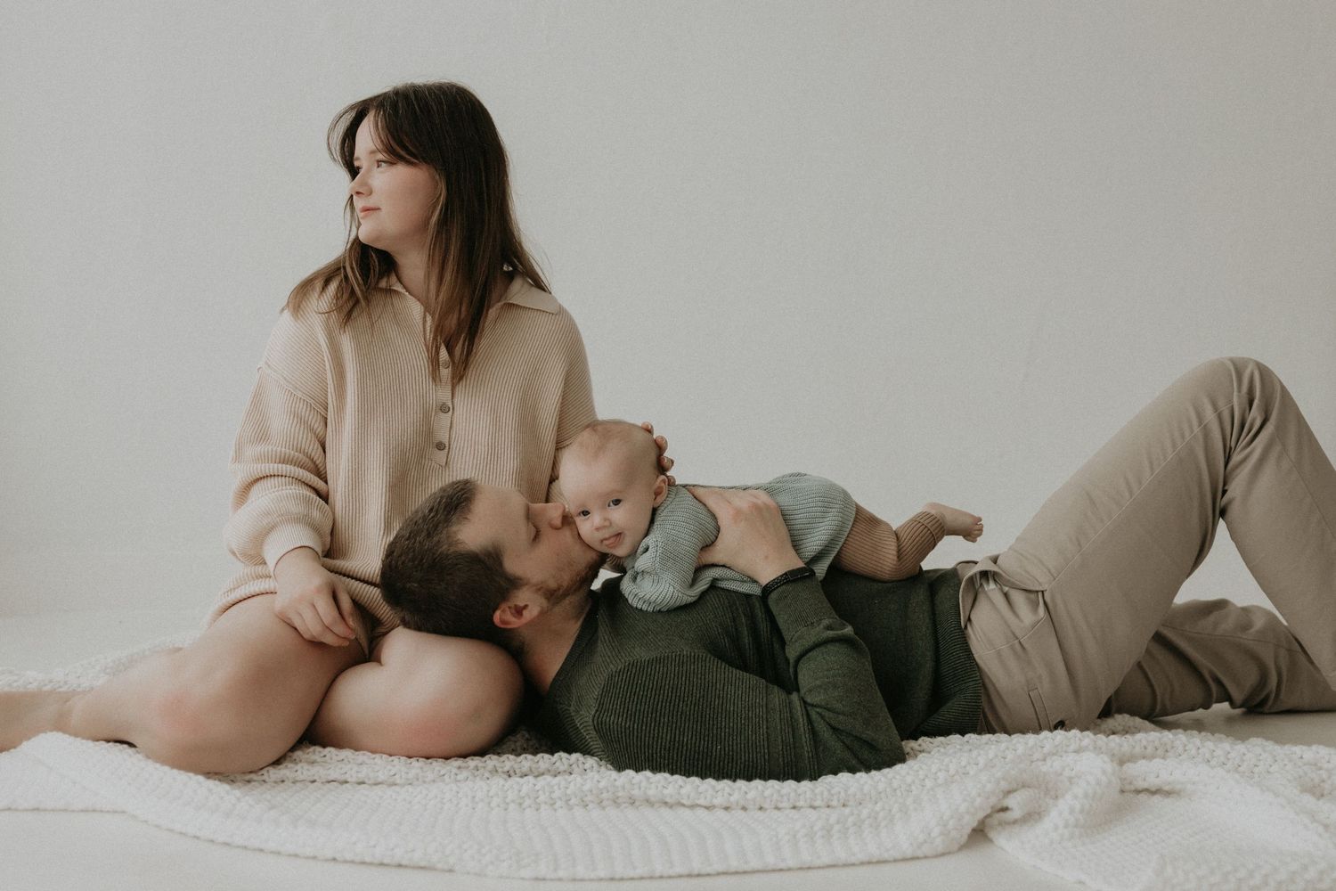 Couple lounging together in neutral tones during intimate indoor photoshoot.