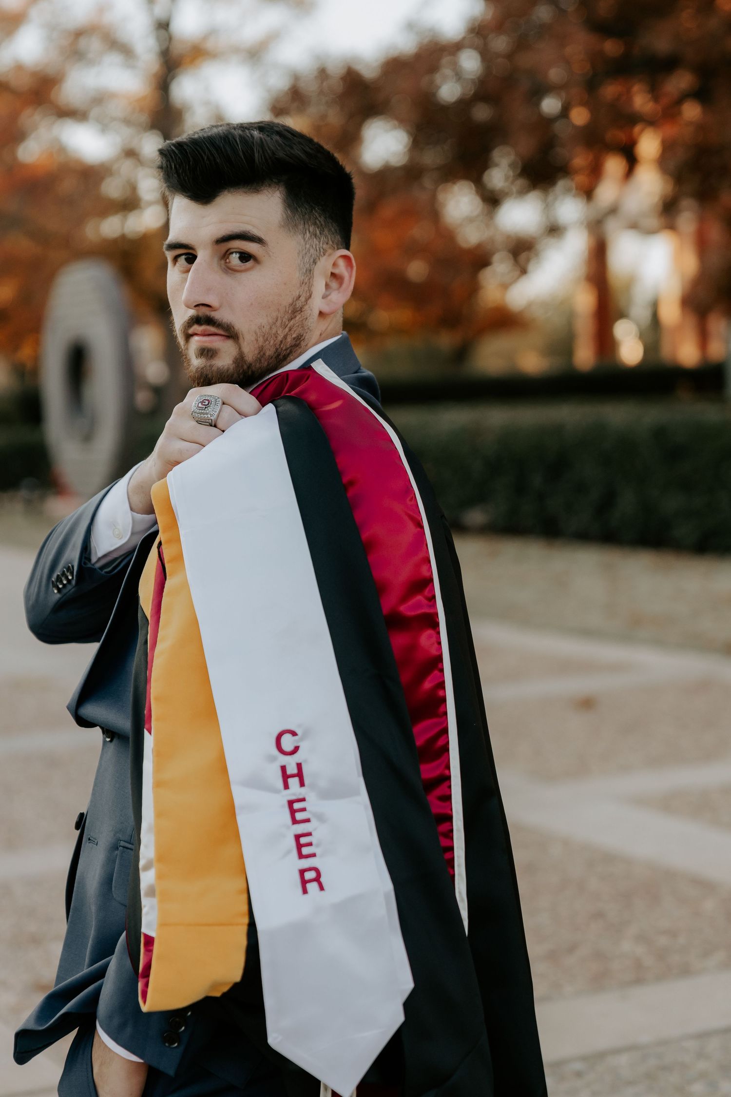 Graduate wearing academic stoles poses outdoors during autumn graduation photoshoot.