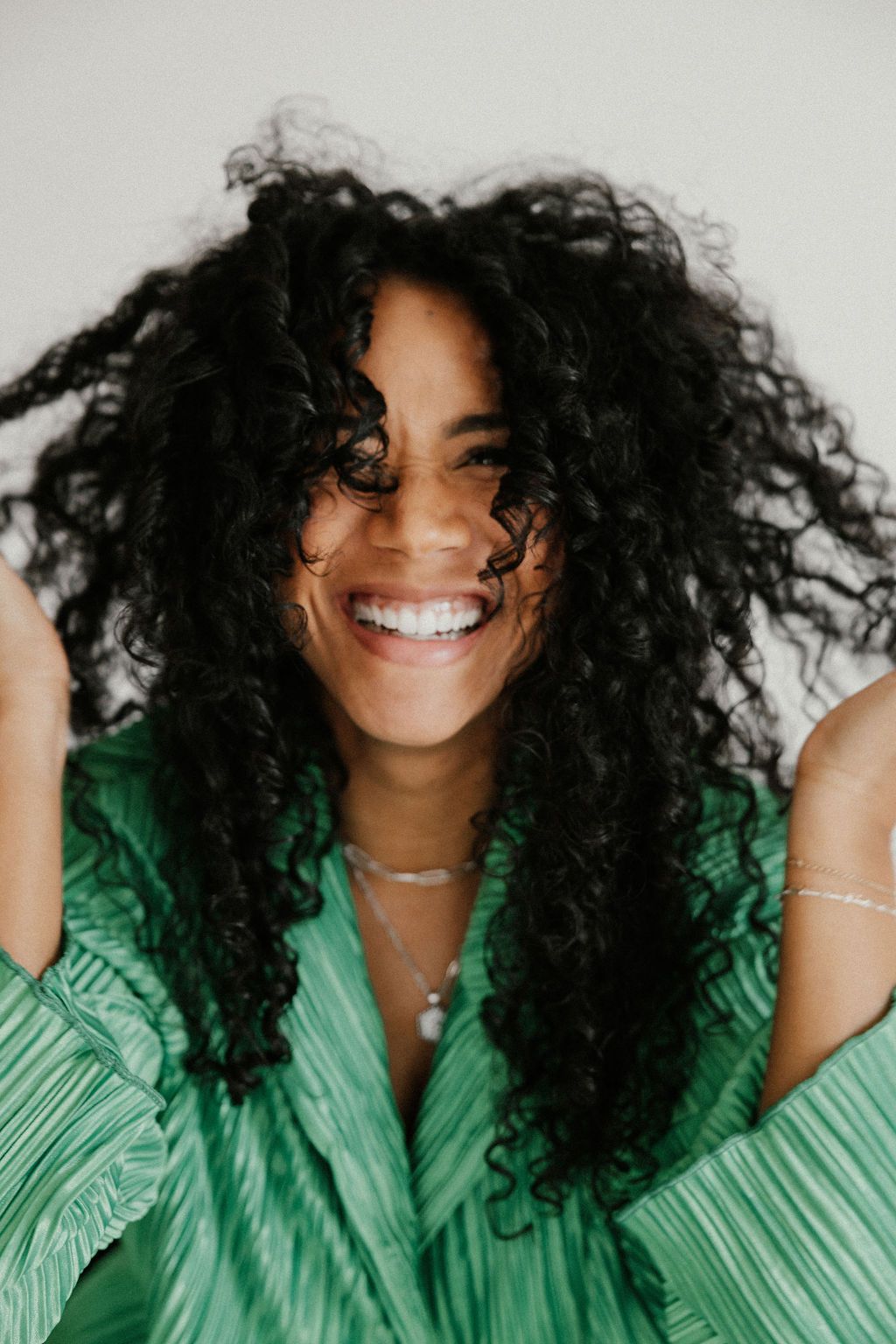 Portrait of a joyful person with natural curly hair wearing a green top against a light background.