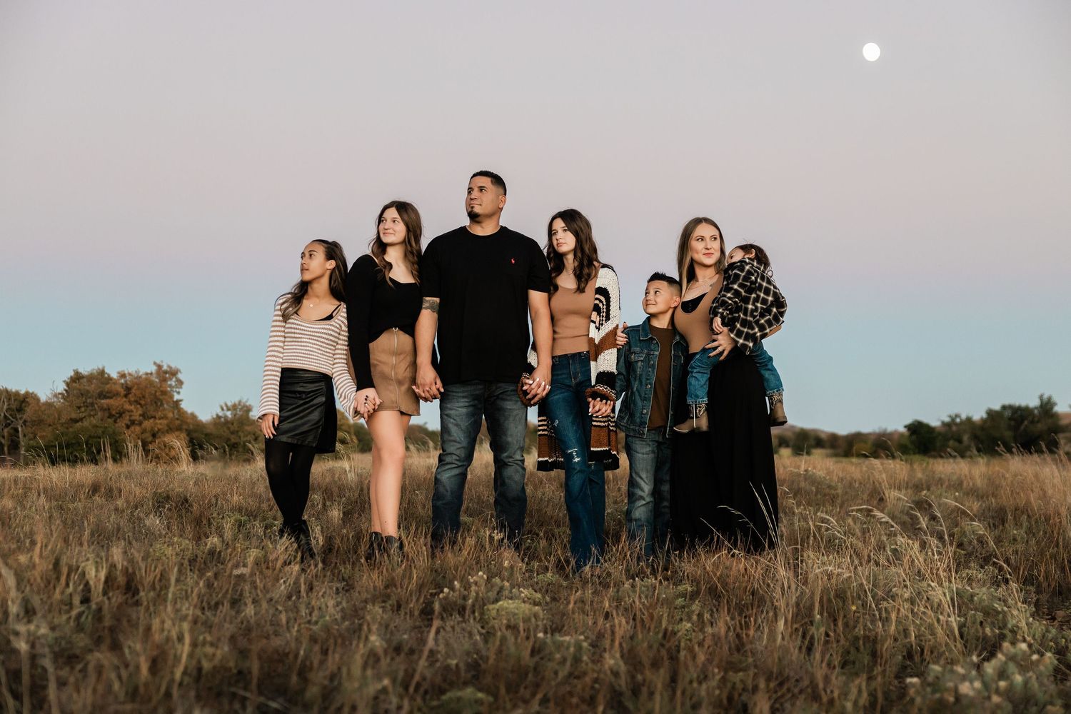 Family members standing together on a grassy hill during twilight.