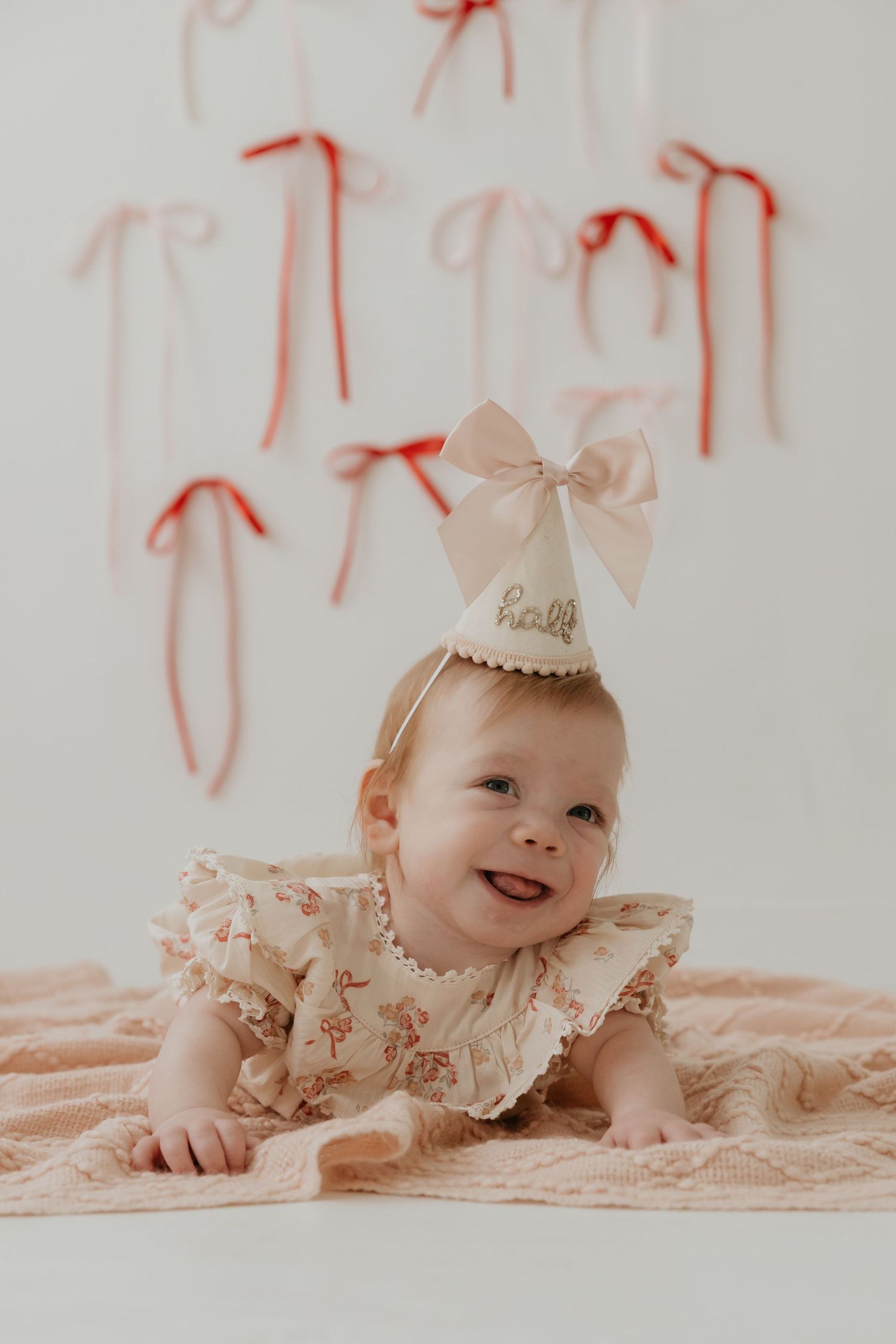 Baby wearing a pink bow and lace dress lying on soft fabric.