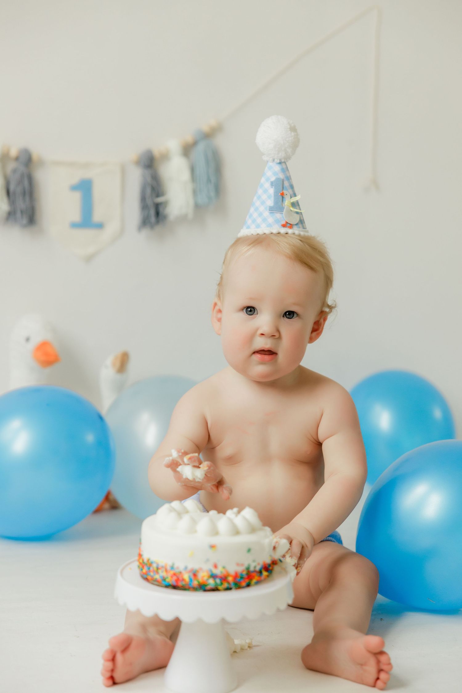First birthday cake smash session with blue balloons and white frosted cake.