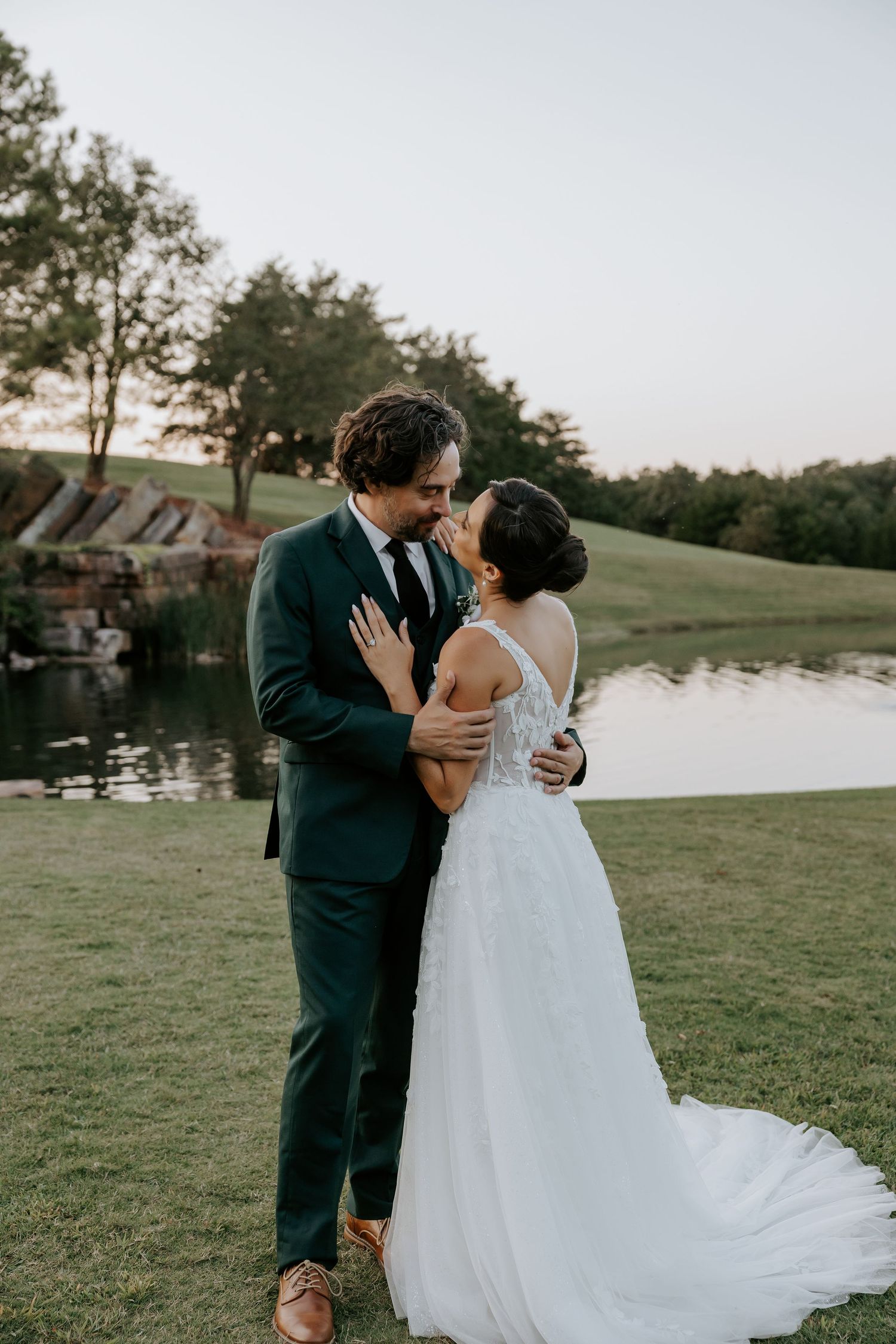 Romantic lakeside moment between newlyweds on grassy shore at sunset.