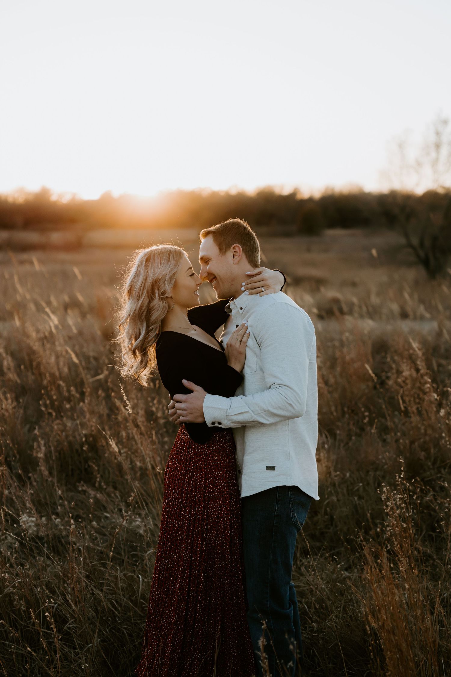 Couple embracing in a golden field during sunset wearing contrasting white and dark outfits.