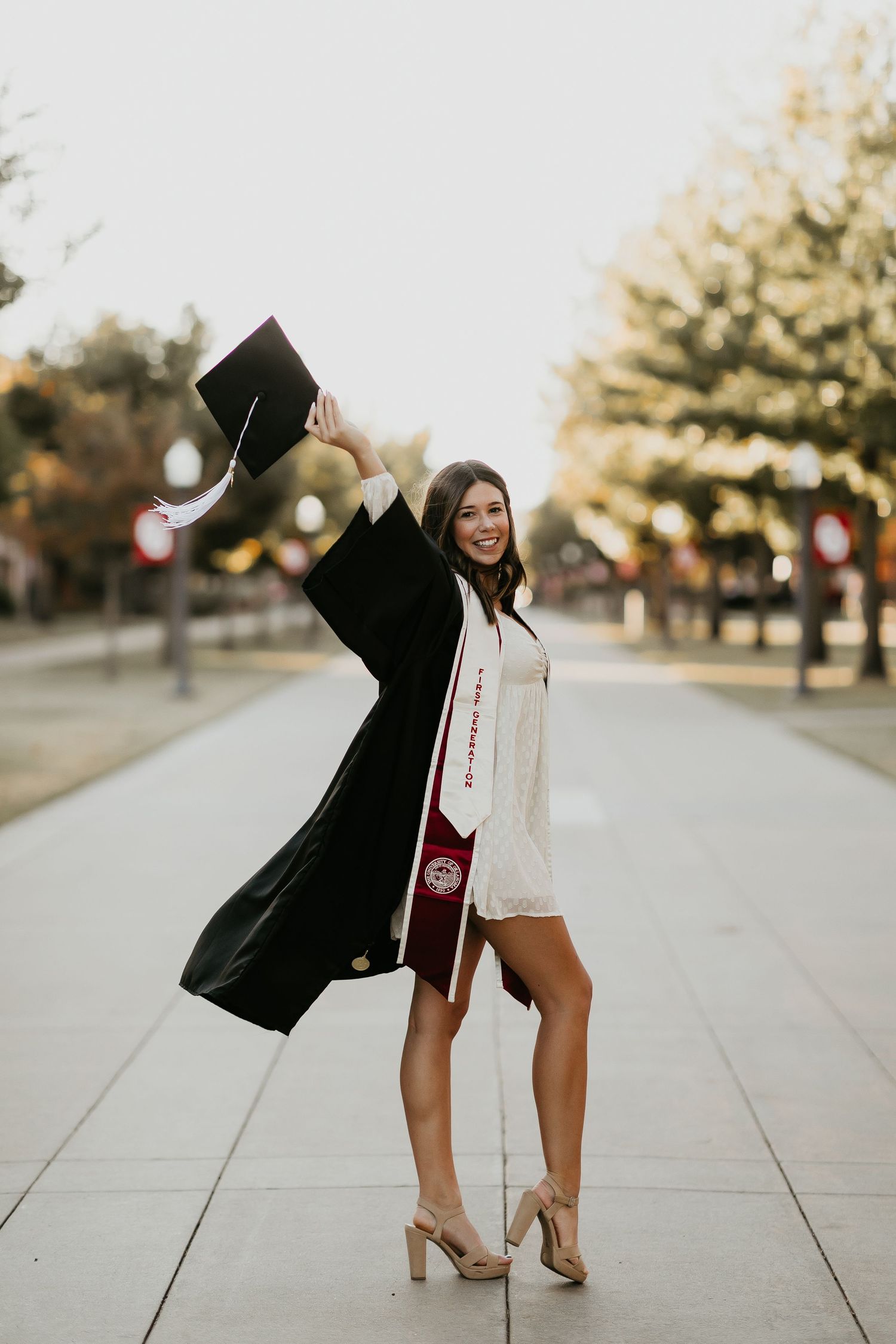 Graduate celebrates by throwing cap in the air on campus walkway.