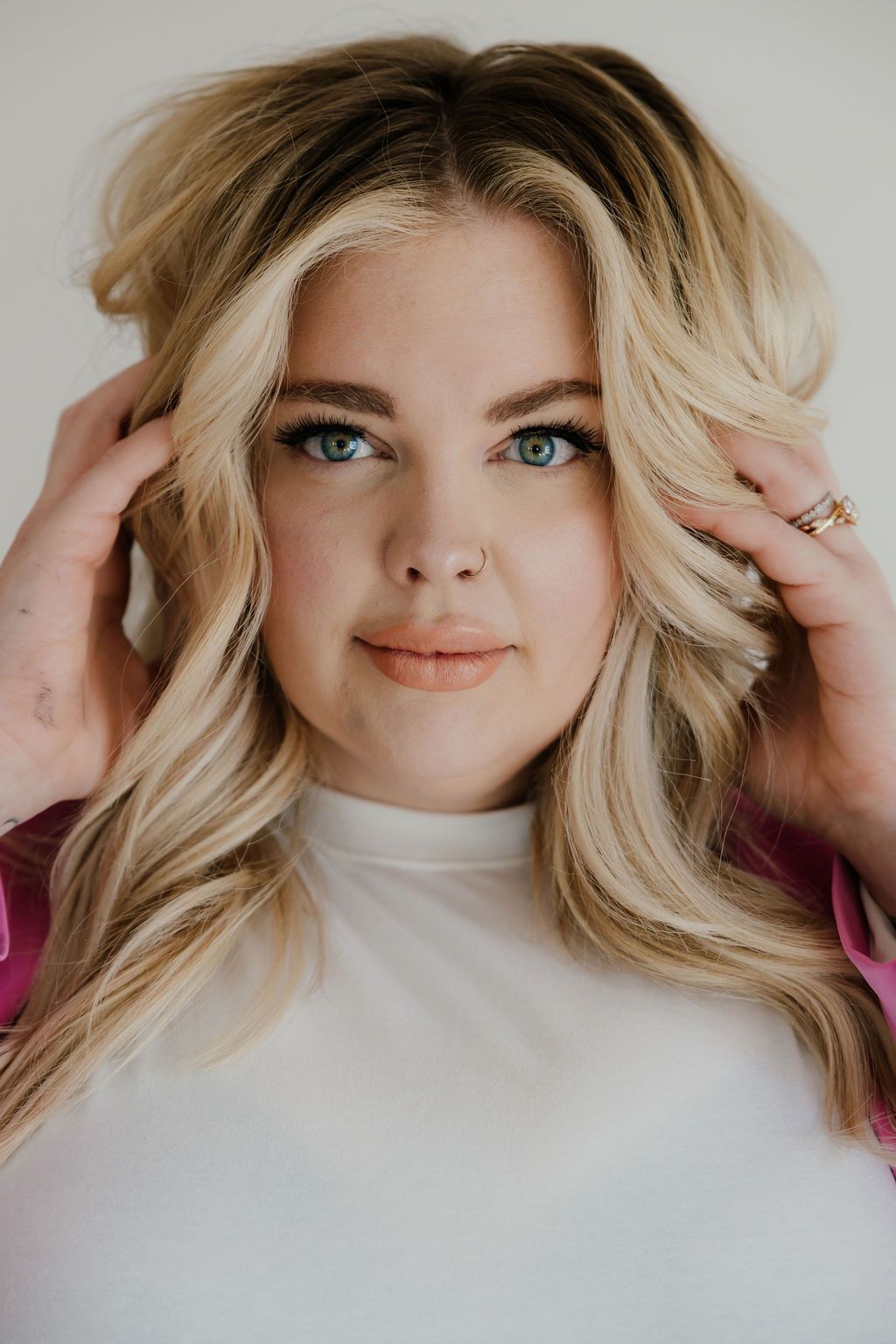 Close-up beauty portrait with hands framing face against white background.