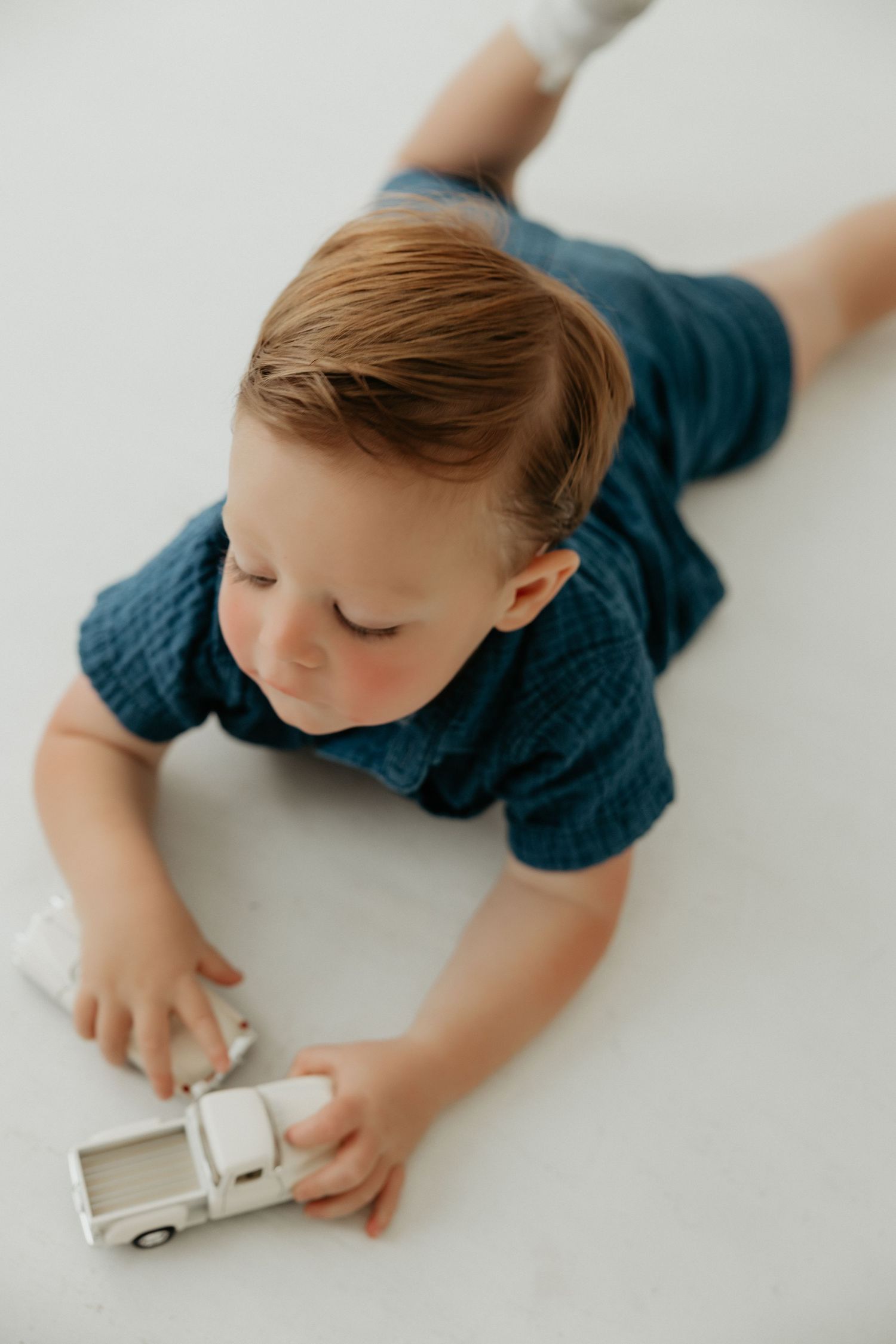 Child in navy blue shirt playing with a toy car on white surface.