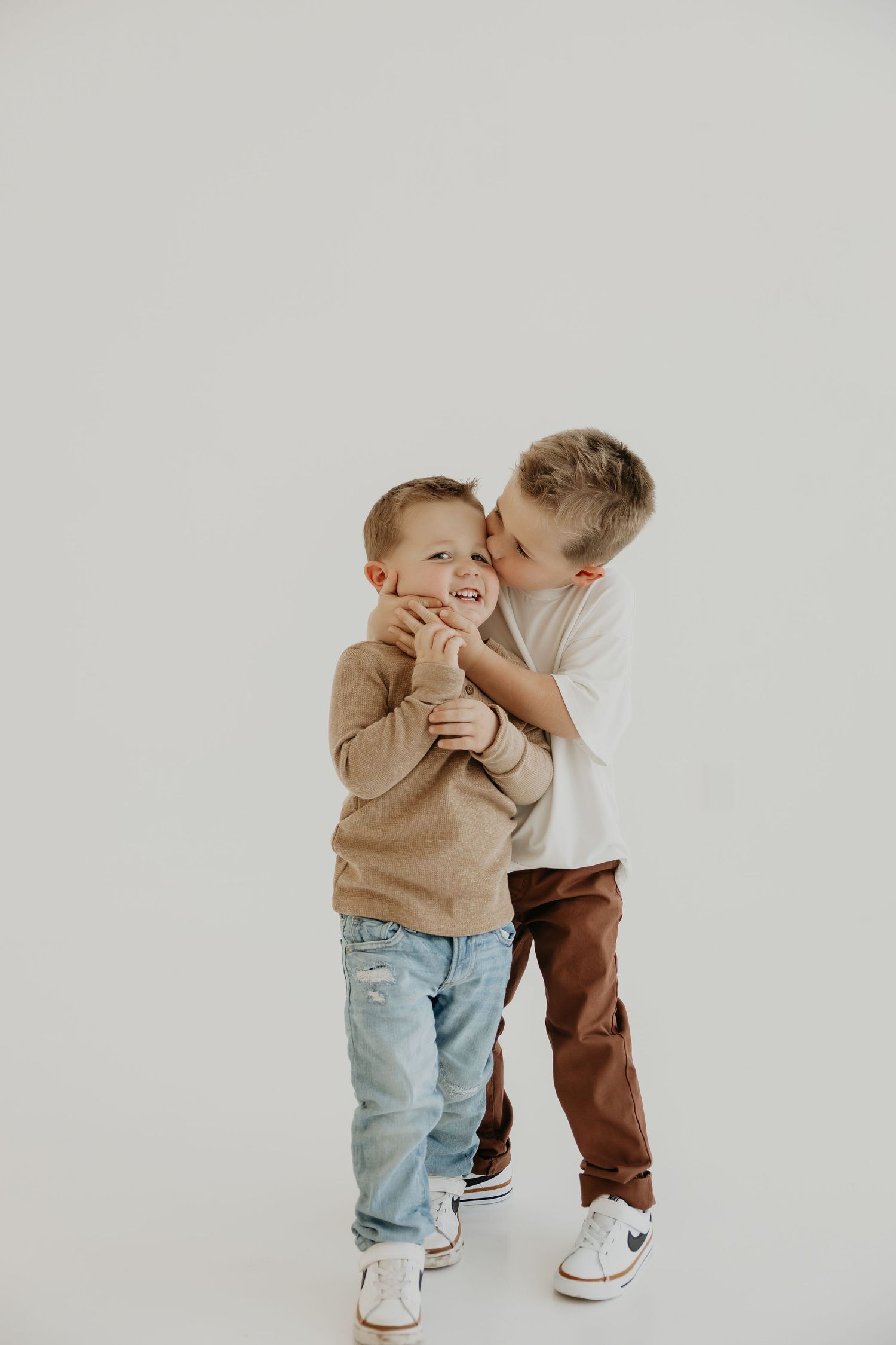 Two young children playing and interacting in casual wear against white studio backdrop.