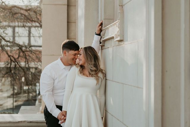 Romantic couple in white outfits sharing intimate moment against stone building.
