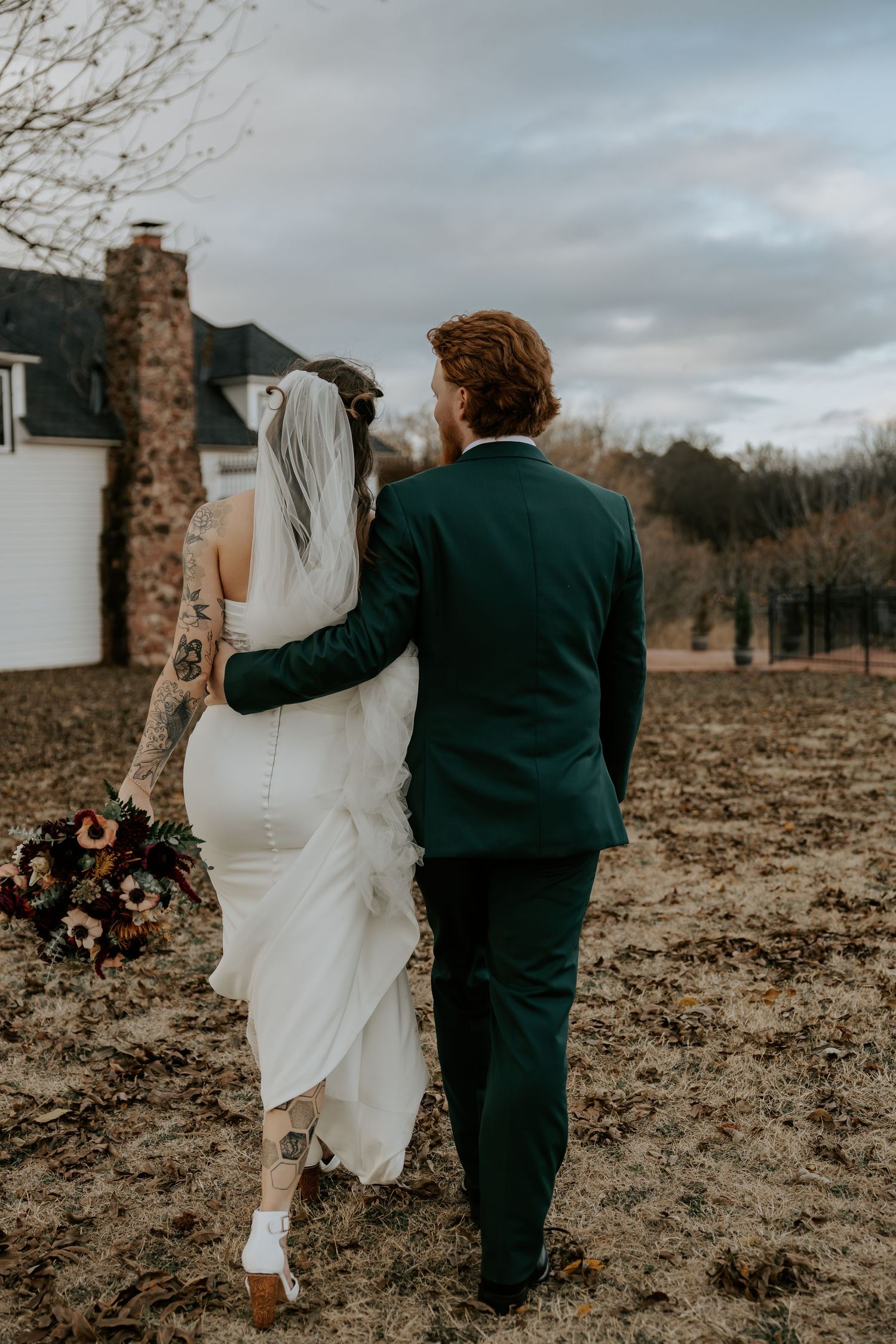Couple walks through bare field holding each other in moody overcast lighting.