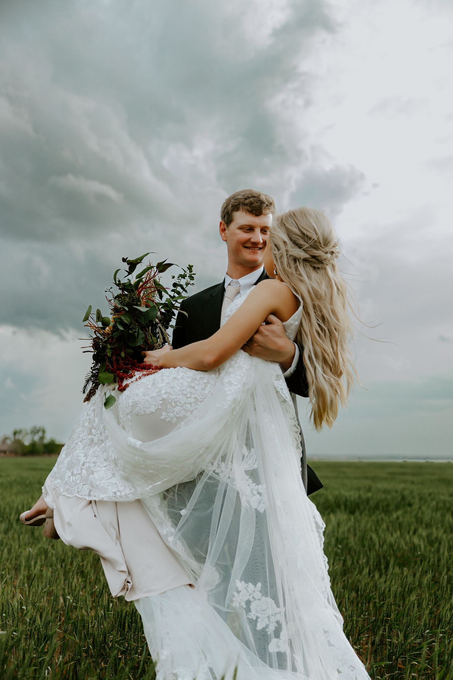 Joyful couple spins together in a green field under dramatic cloudy skies.