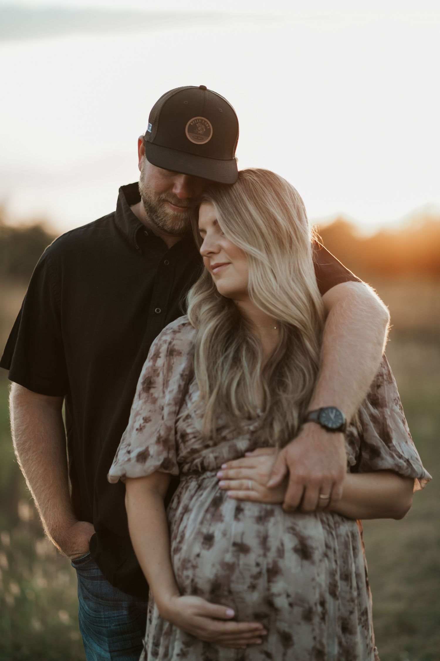 Couple embracing during sunset maternity photoshoot in outdoor setting.