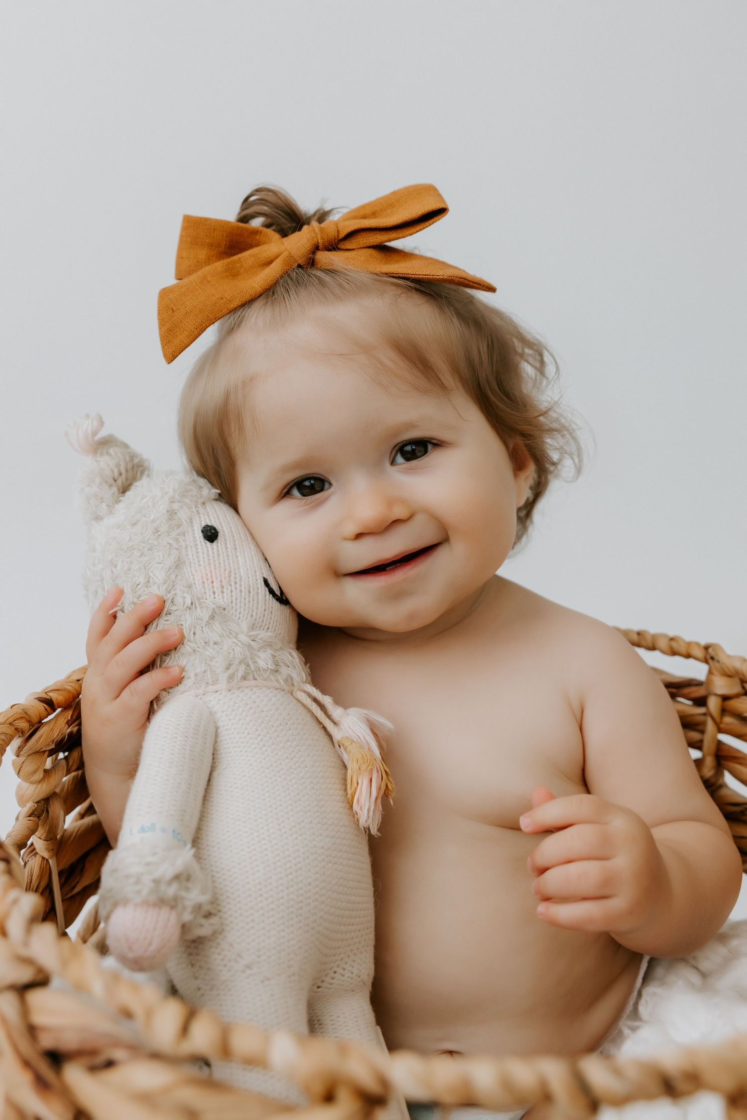 Baby sitting in woven basket with stuffed bunny toy and orange bow.