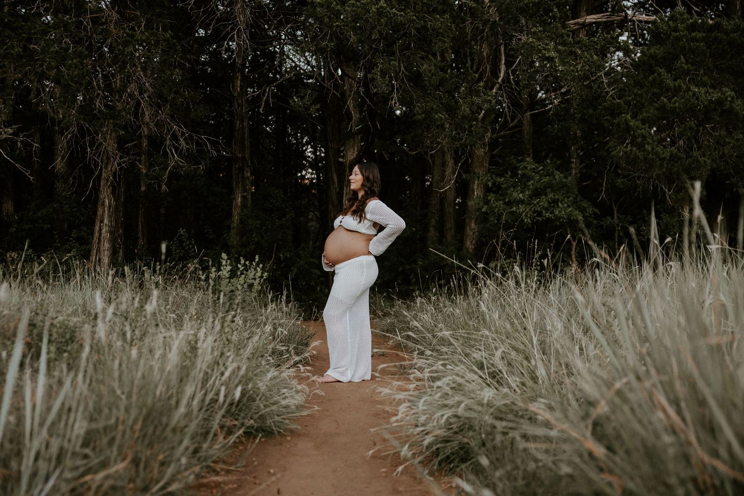 Outdoor maternity photoshoot in a natural wooded setting with tall grass.
