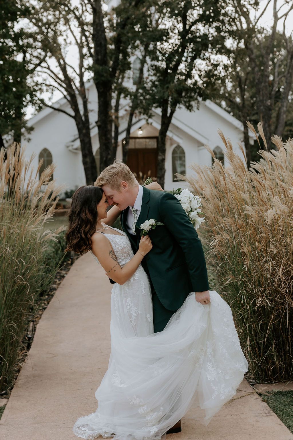 Romantic wedding couple embracing on path surrounded by ornamental grasses.