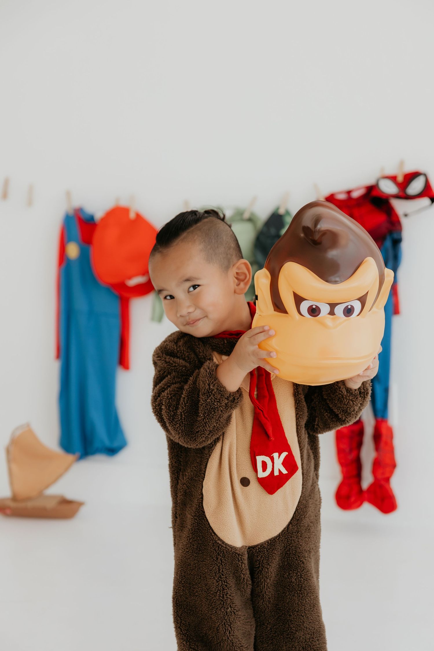 Child wearing Donkey Kong costume plays with character mask.