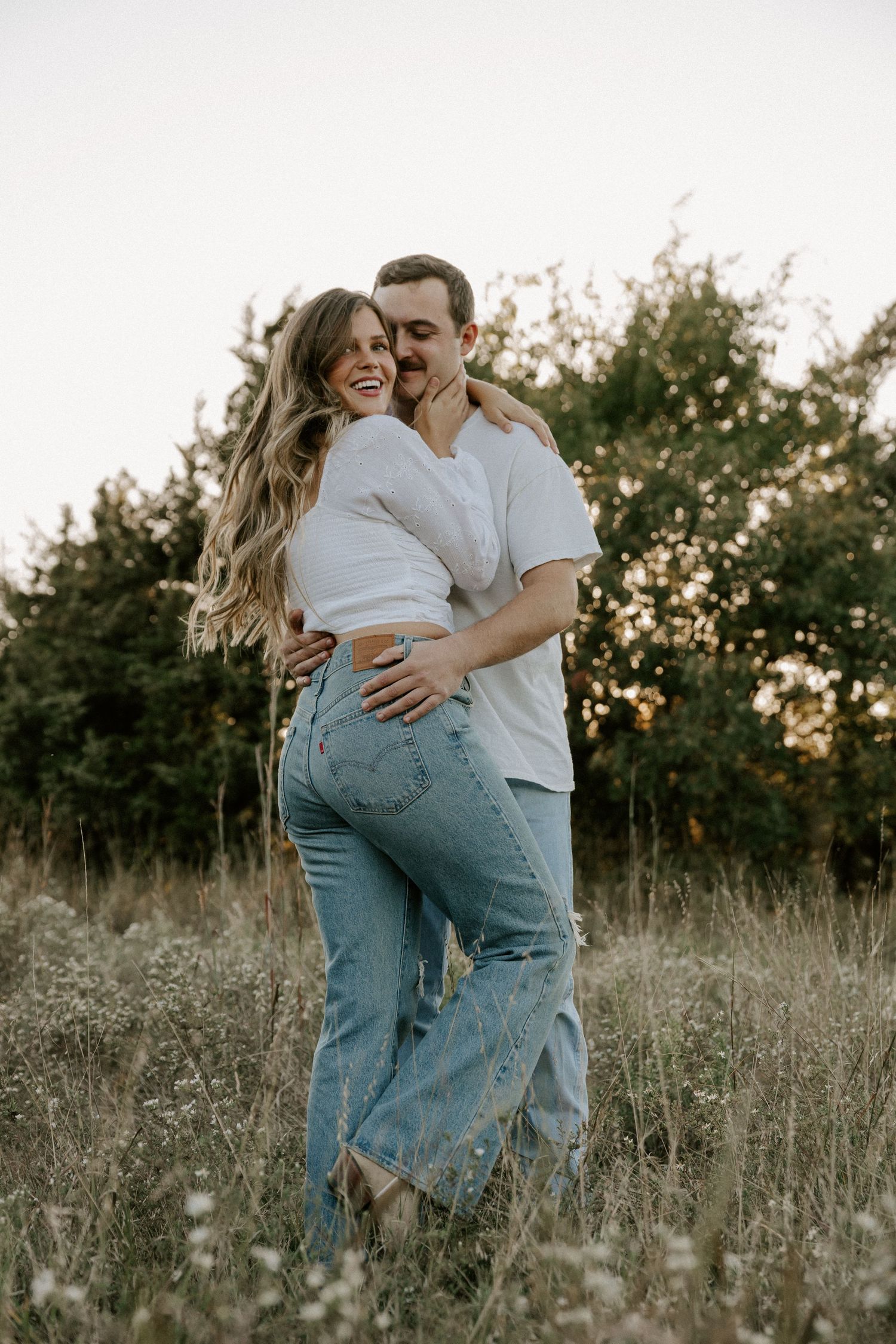 Candid portrait of laughing couple in casual wear embracing in golden hour light.