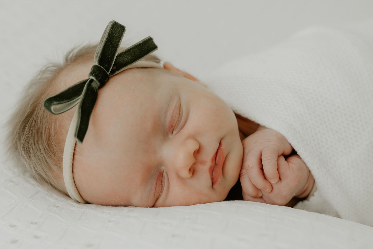 Peaceful newborn sleeping soundly against white bedding with a delicate bow accessory.