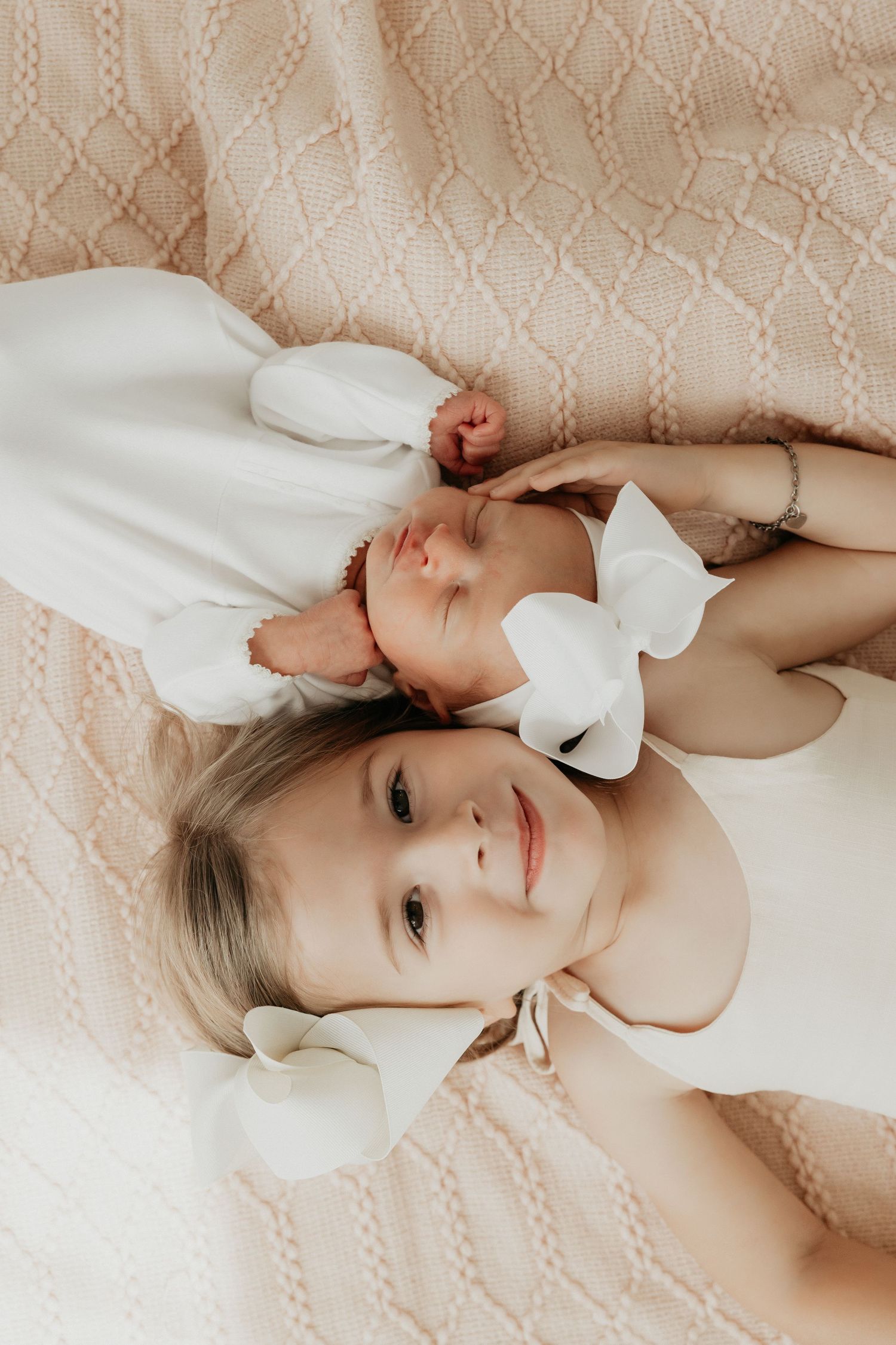 Baby lying on textured beige bedding wearing white outfit.